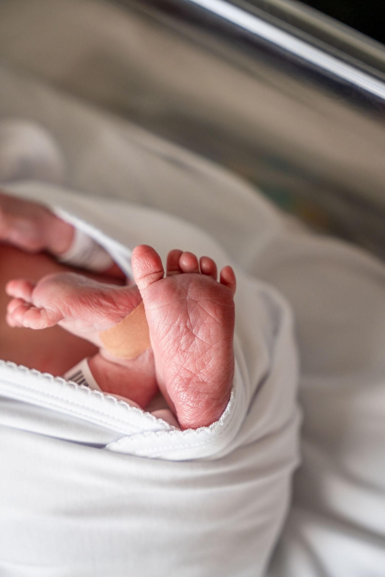 Close-up of newborn baby feet resting on white hospital blanket.