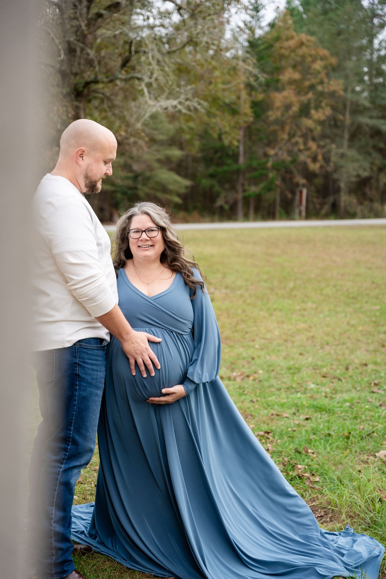 A couple poses together outdoors near rustic grain bins as a blue dress flows in the breeze.