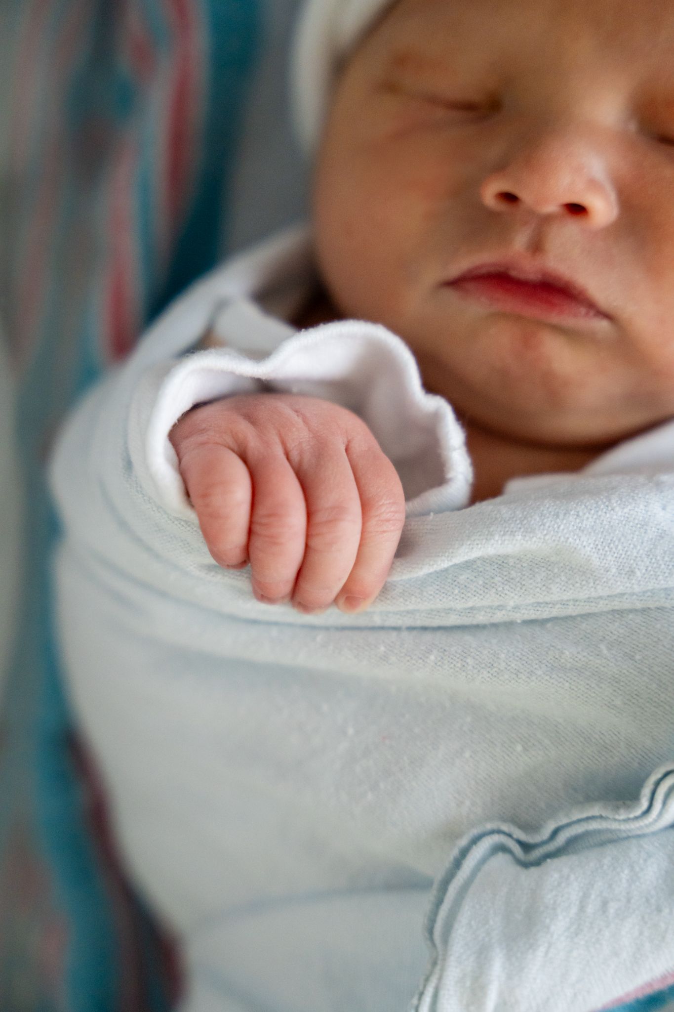 Close-up details of a swaddled newborn infant wrapped in soft white fabric.