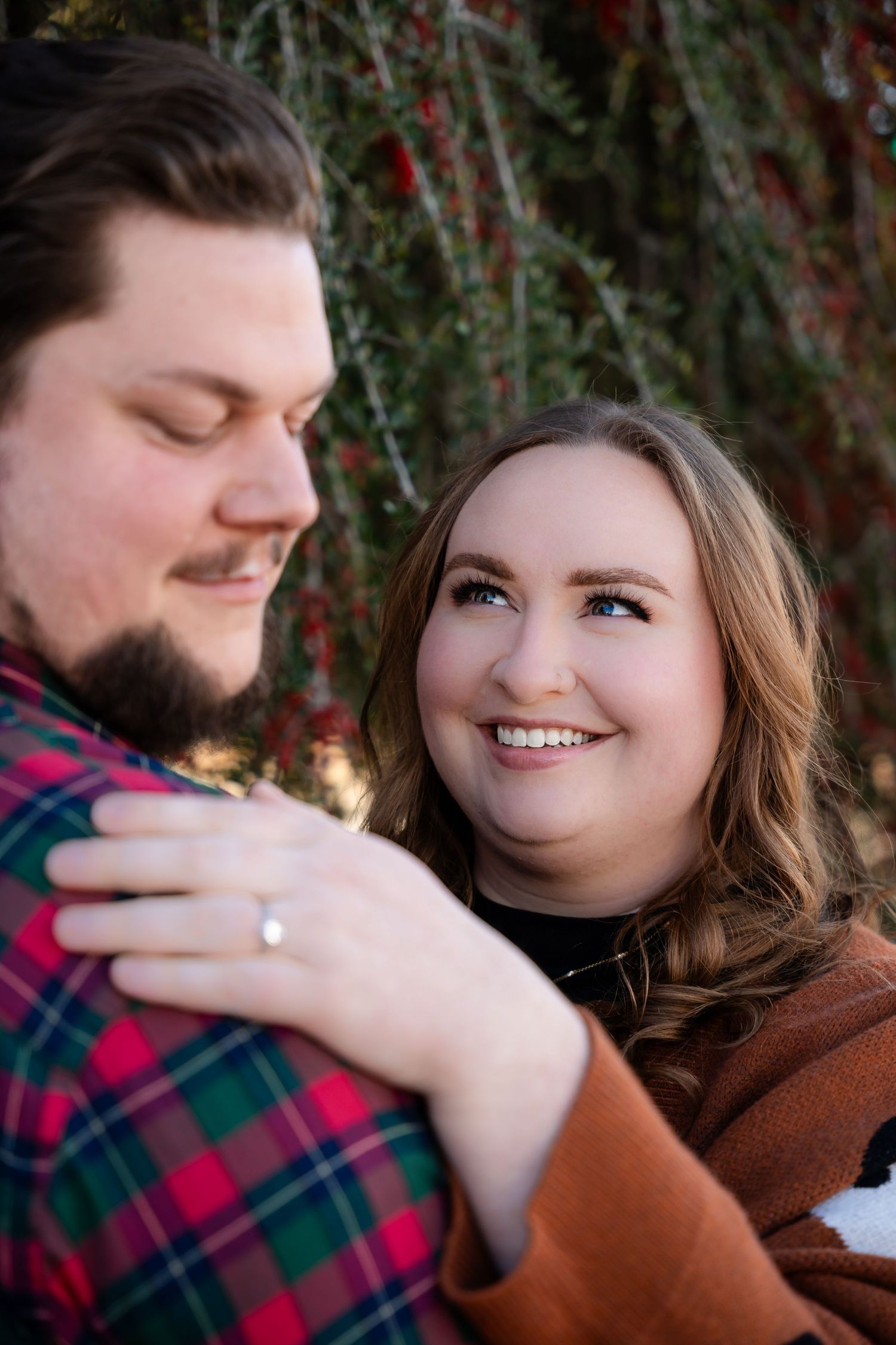 Close-up engagement ring shot with couple in background.
