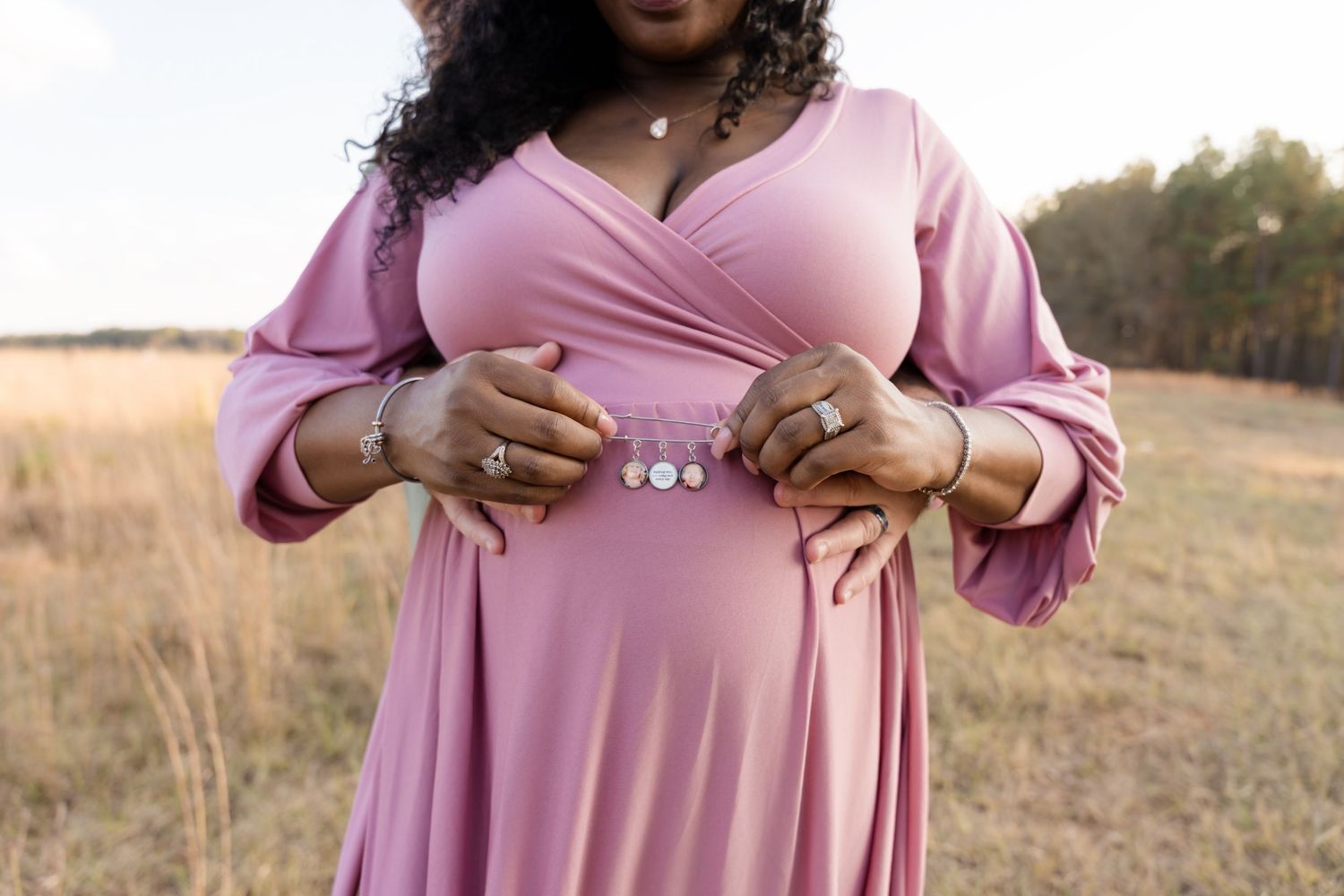 Pregnant woman in pink maxi dress holding baby bump in golden field during maternity photo shoot.