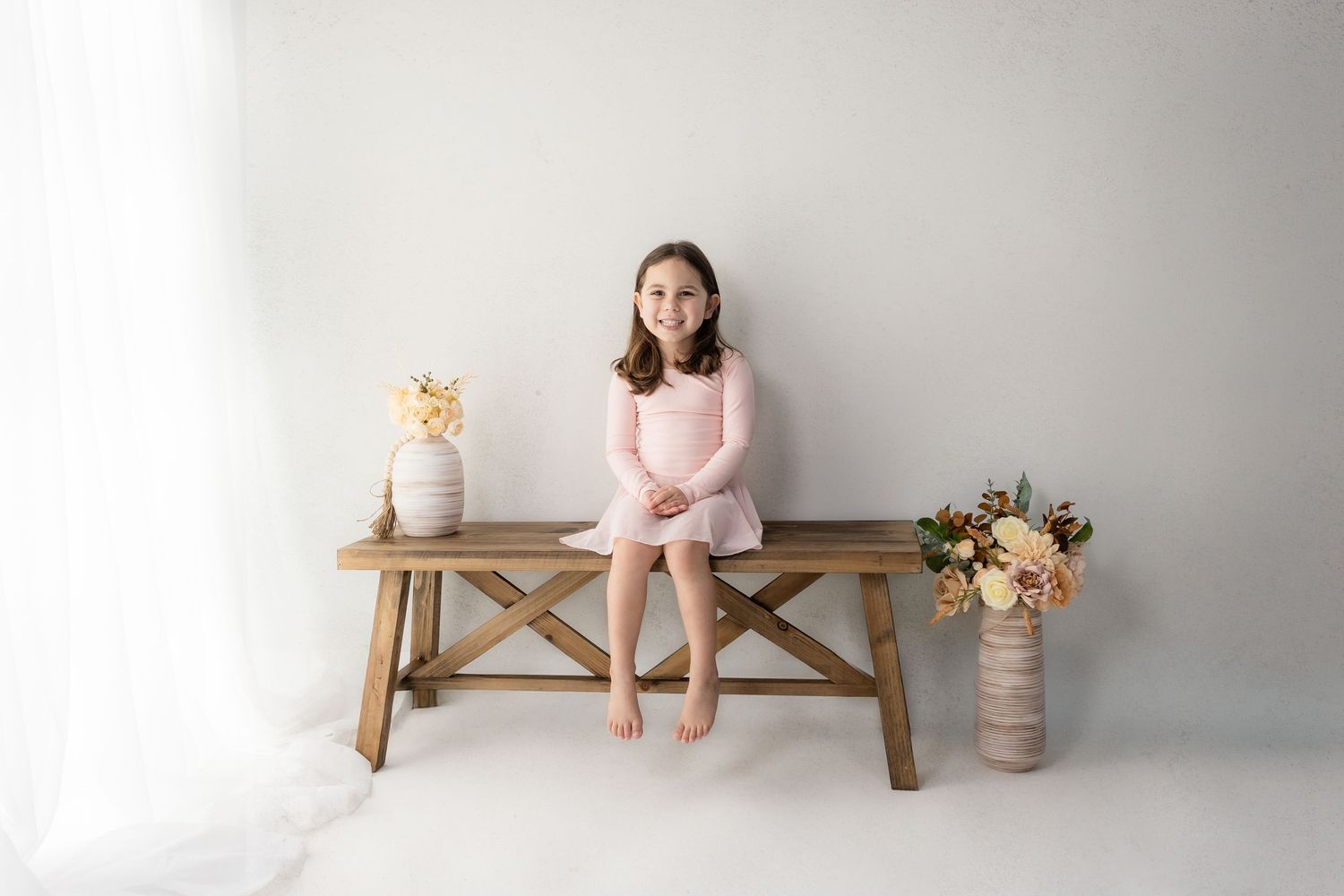 Simple wooden bench setup against white wall with soft pink decorative elements.