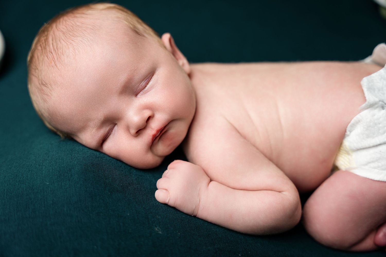 Peaceful newborn resting on dark teal backdrop with white fabric details.
