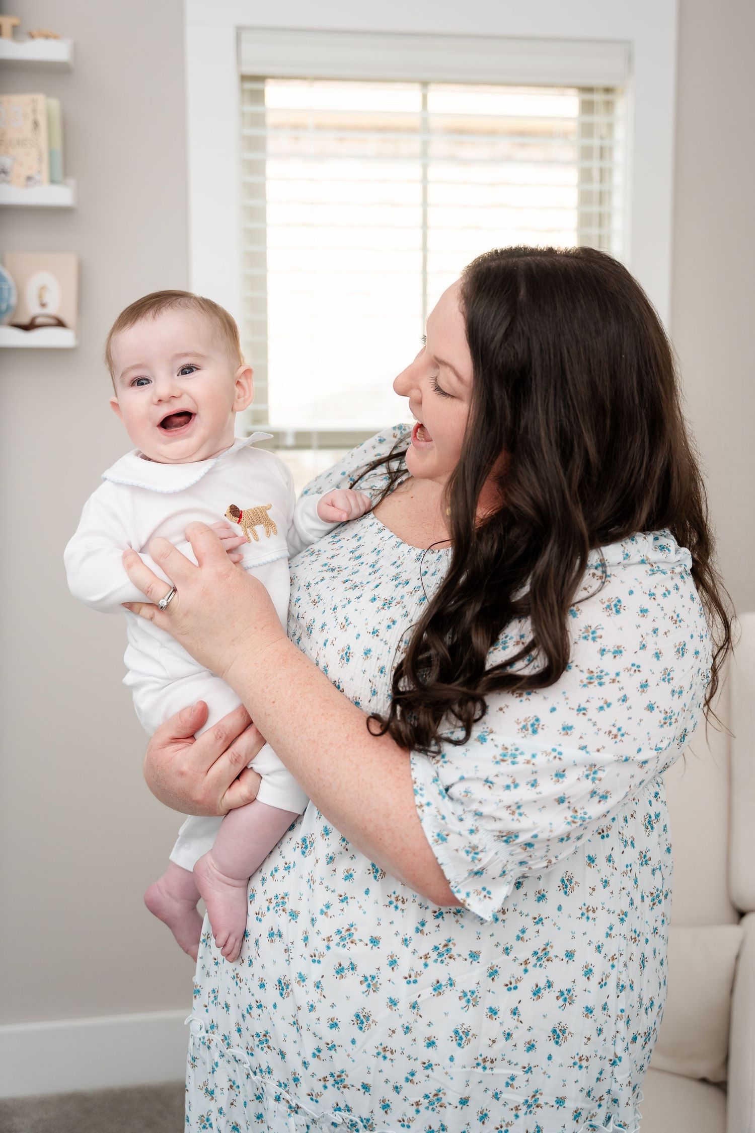 A tender moment captured as a woman in floral dress lifts a laughing baby wearing white.