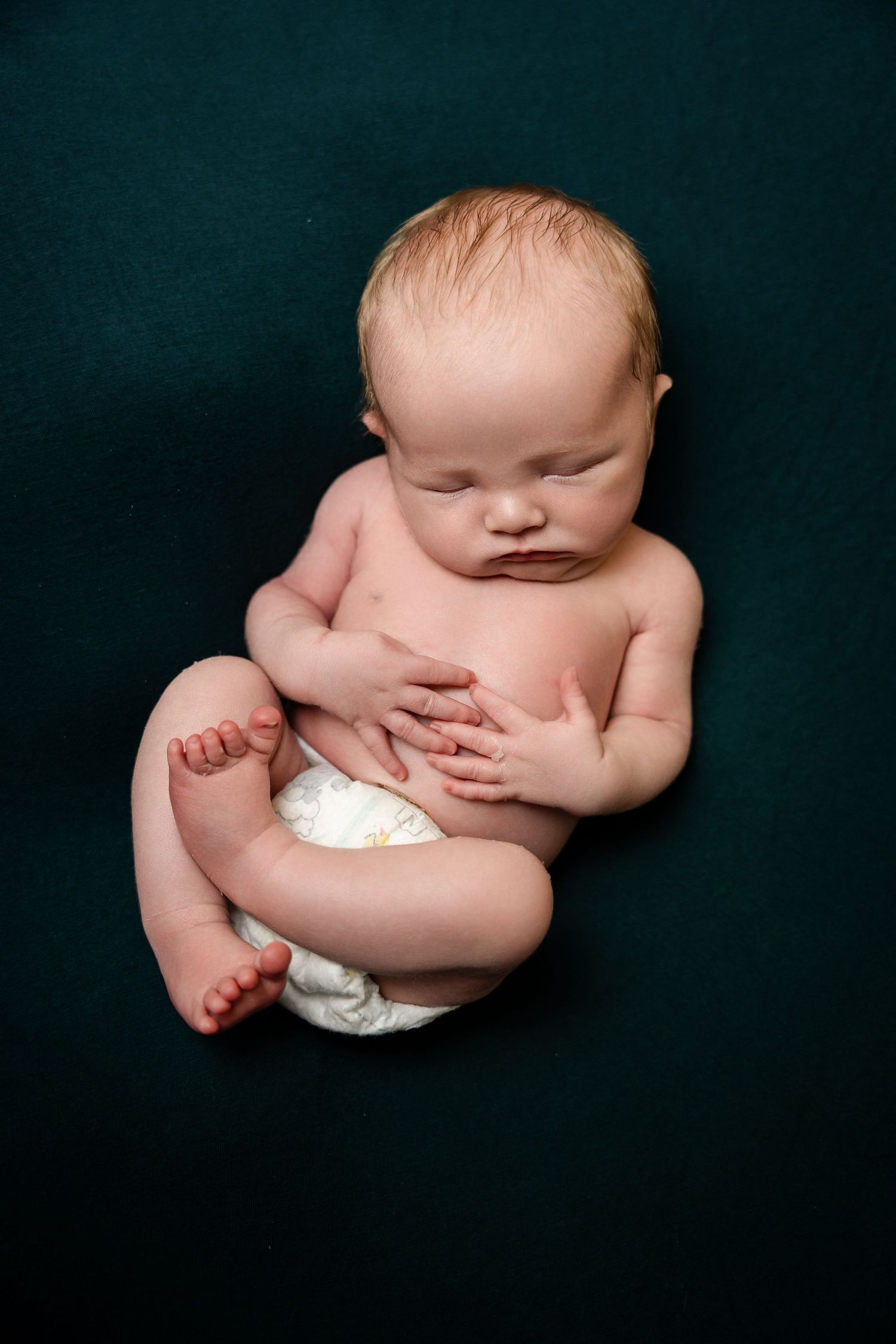 Artistic studio portrait of sleeping newborn against dark background.