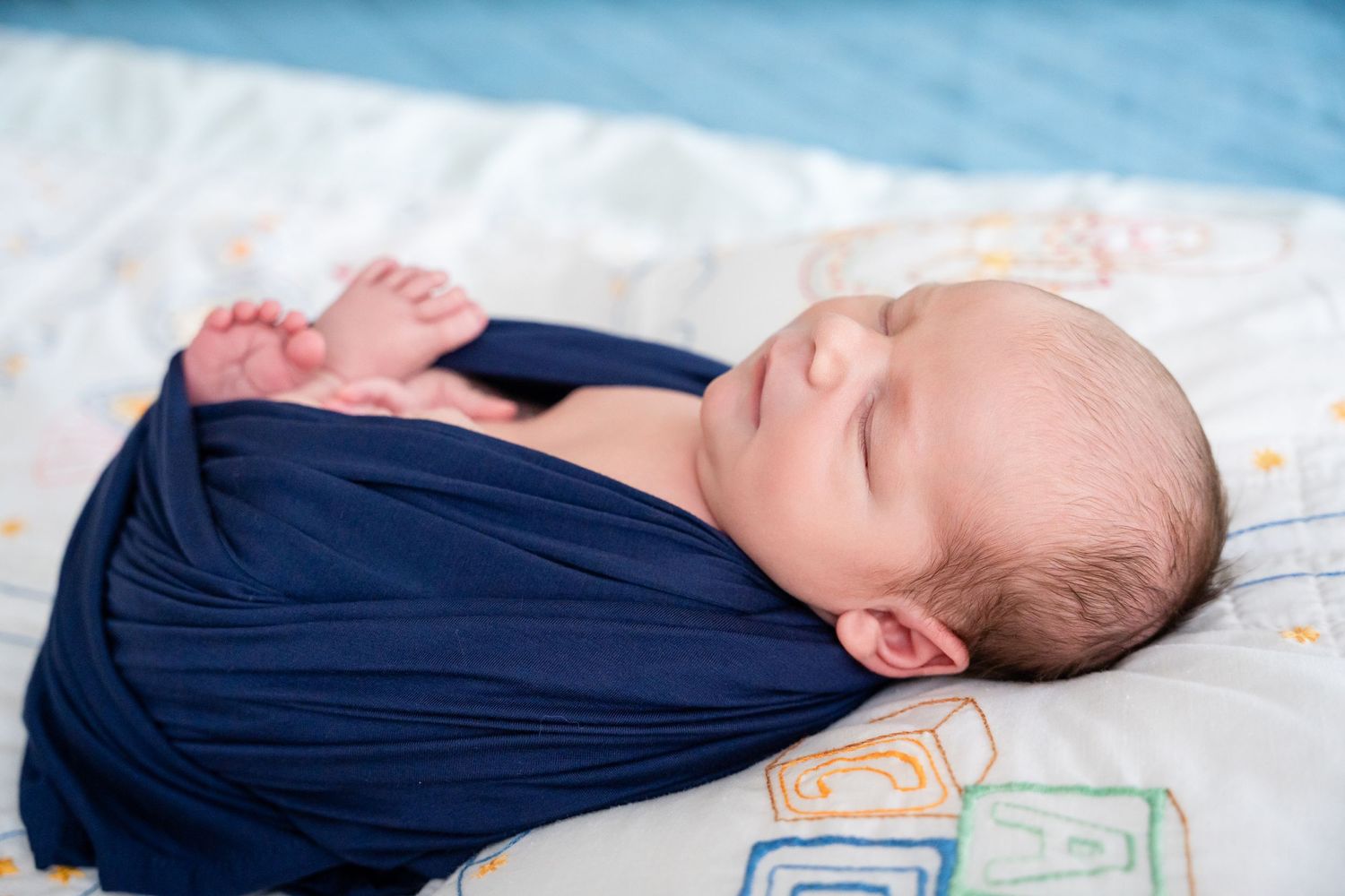 Peaceful infant in navy blue outfit sleeping on patterned bedding.