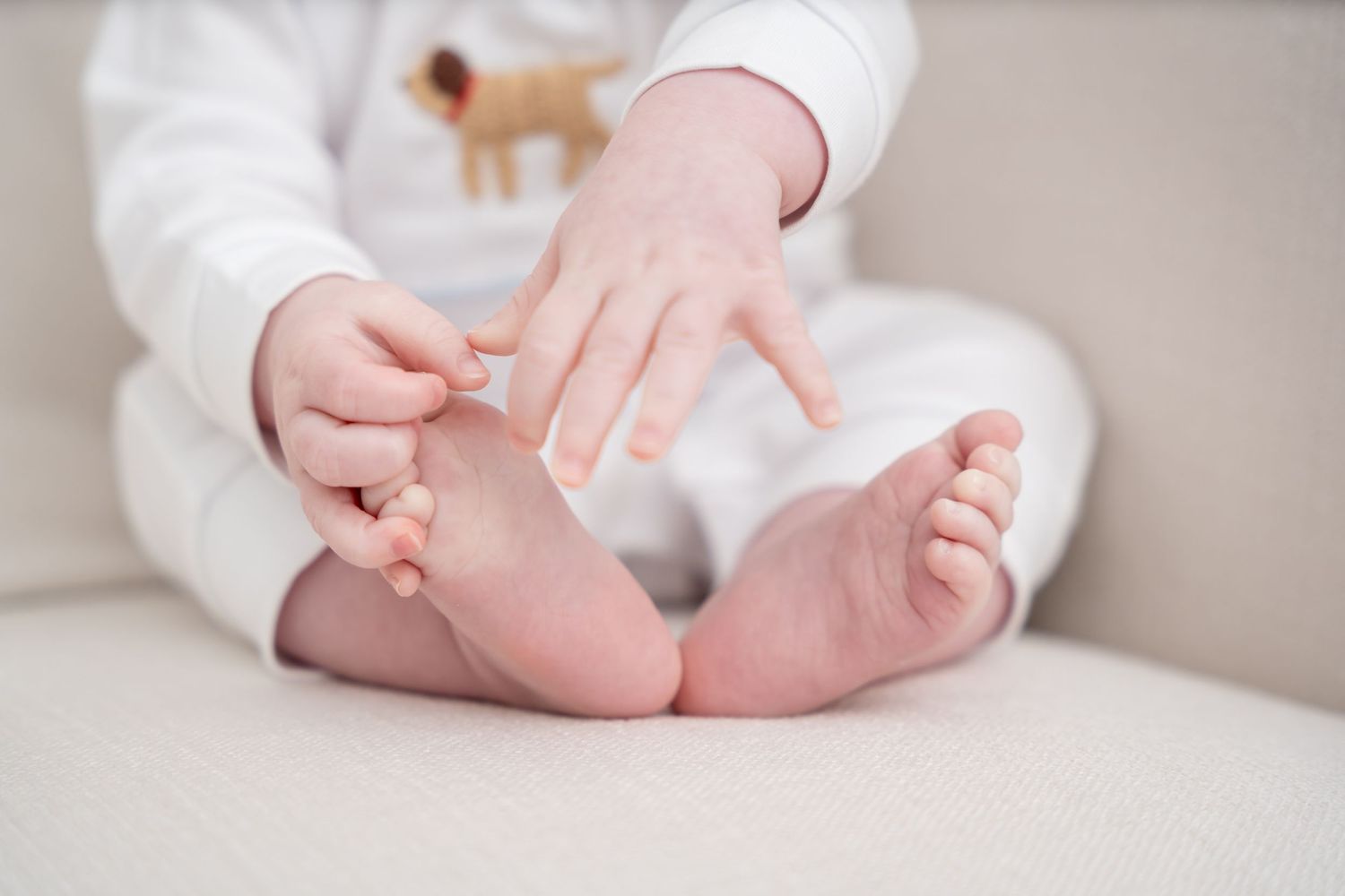 Small baby feet and hands playing on a white couch cushion.