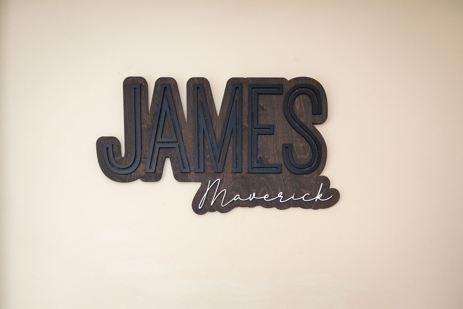 Modern black wall sign displaying 'JAMES' with script lettering against beige wall.