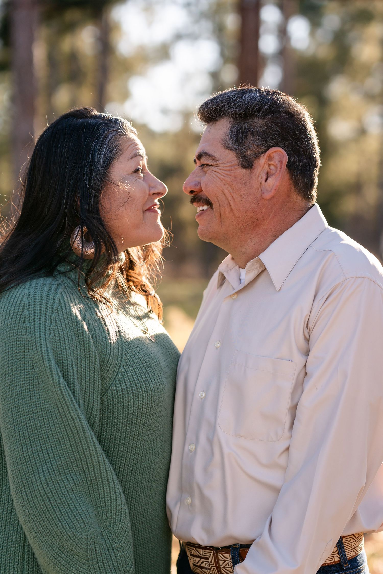 A couple shares a joyful moment together in warm sunset lighting among pine trees.