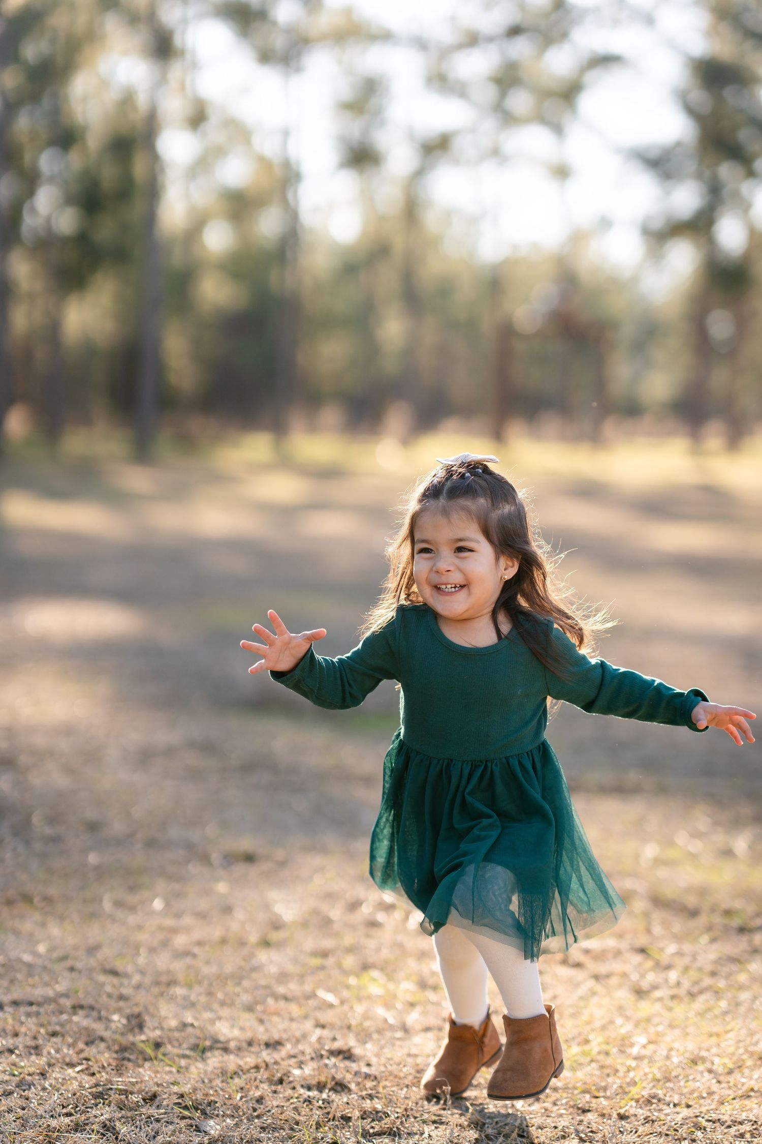 A young child in an emerald green dress plays and dances outdoors during golden hour.