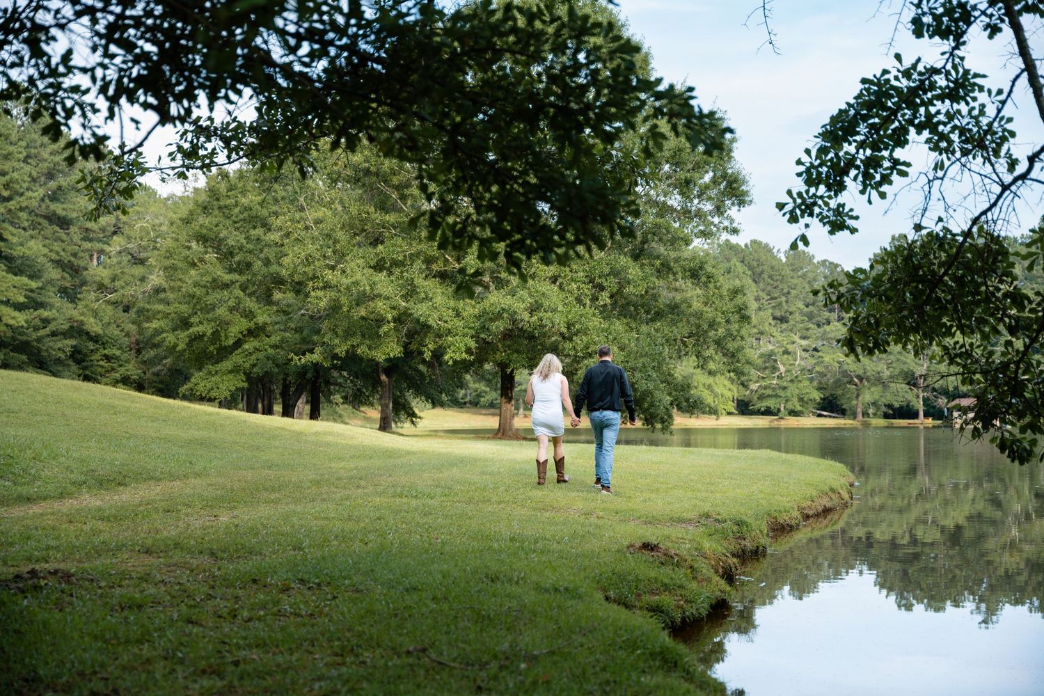 Peaceful pond surrounded by lush green trees and grass on a sunny day.
