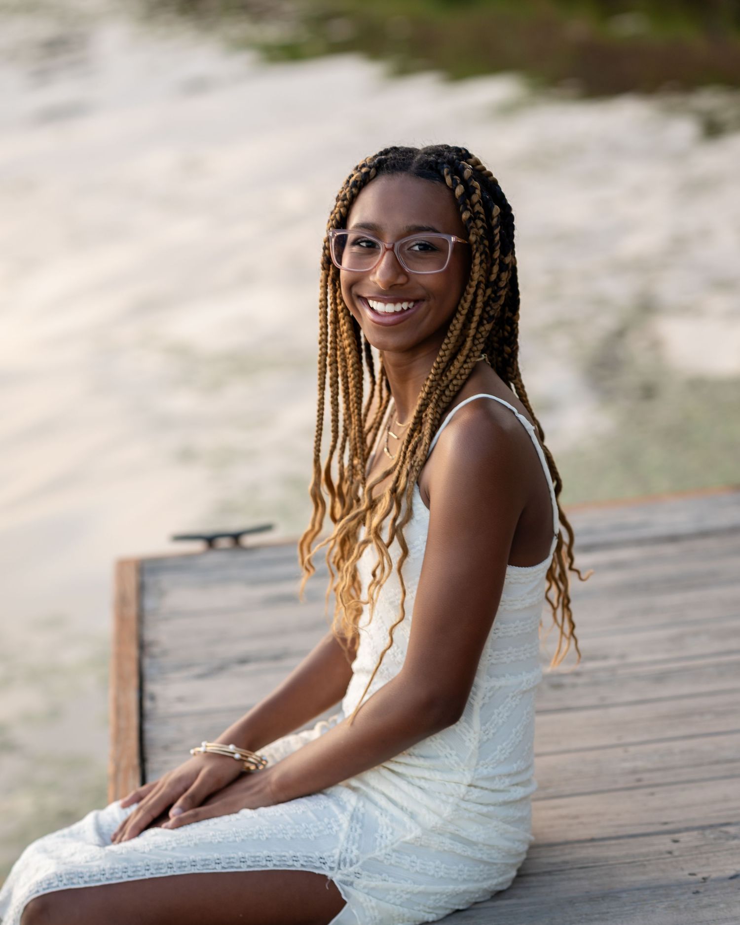 Woman in a white dress sitting on a wooden deck during a photoshoot.