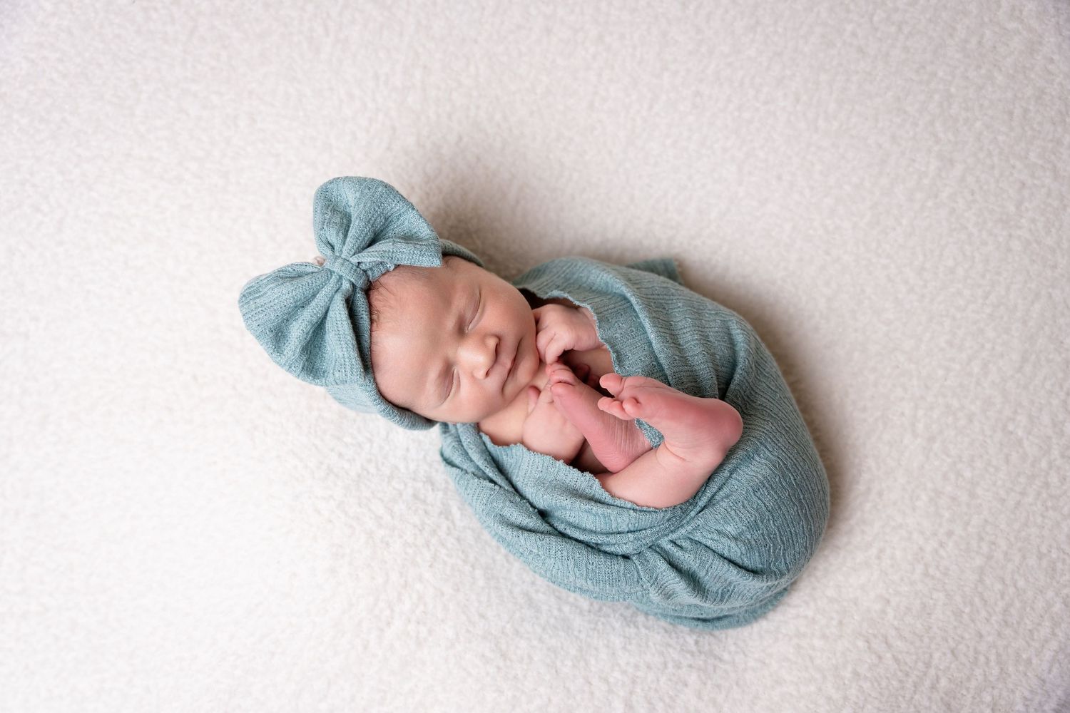 Baby wearing soft blue wrap with matching bow on white background.