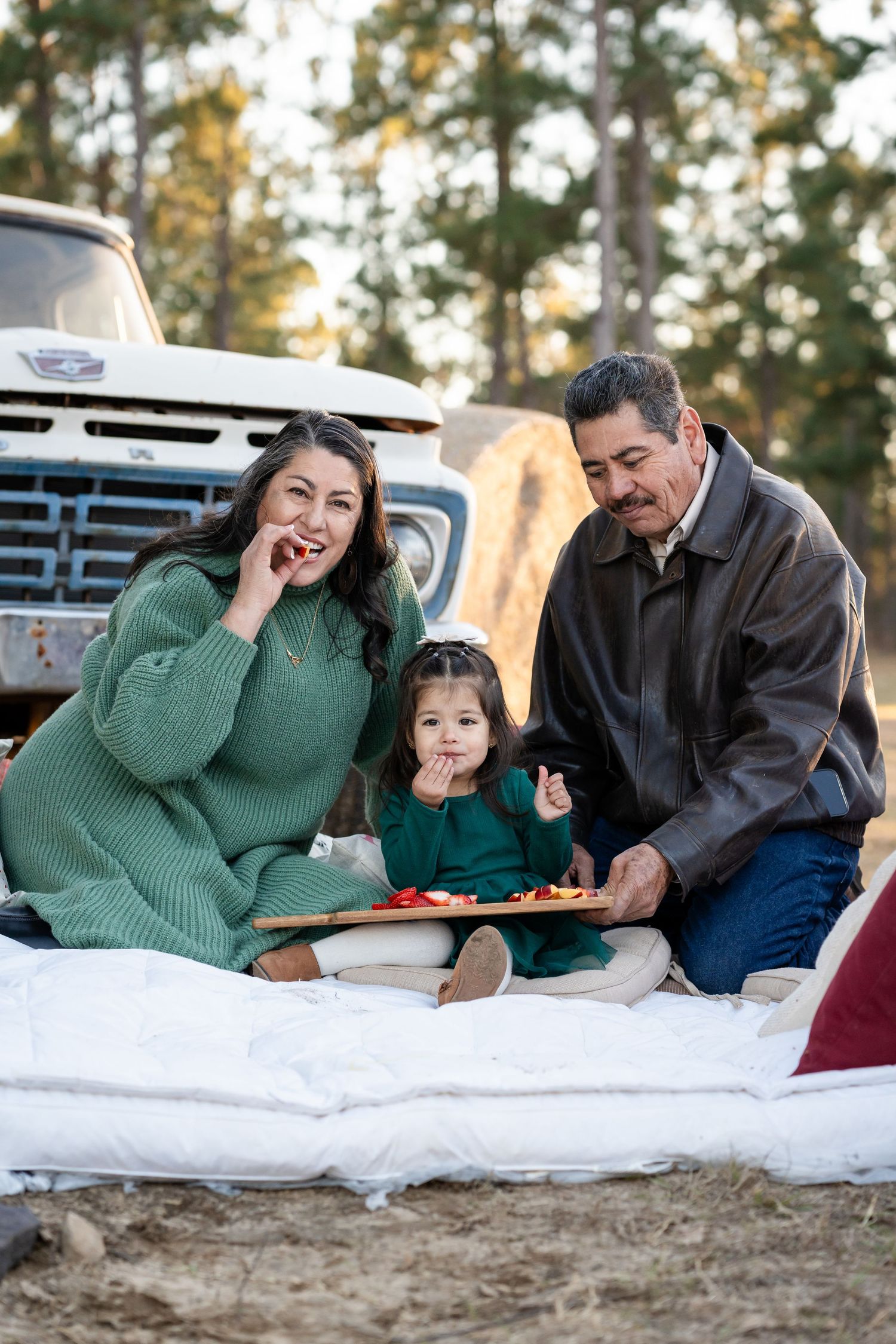 Family sharing snacks and laughing together during outdoor picnic by vintage truck.