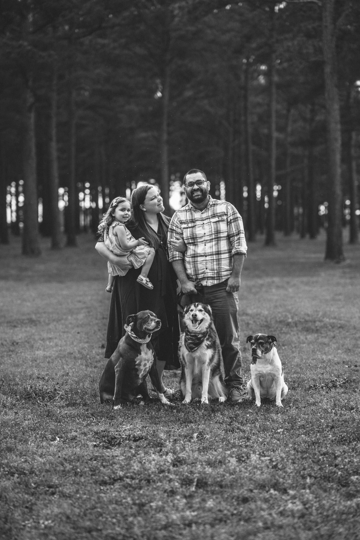 Black and white family photo with dogs in wooded outdoor setting.
