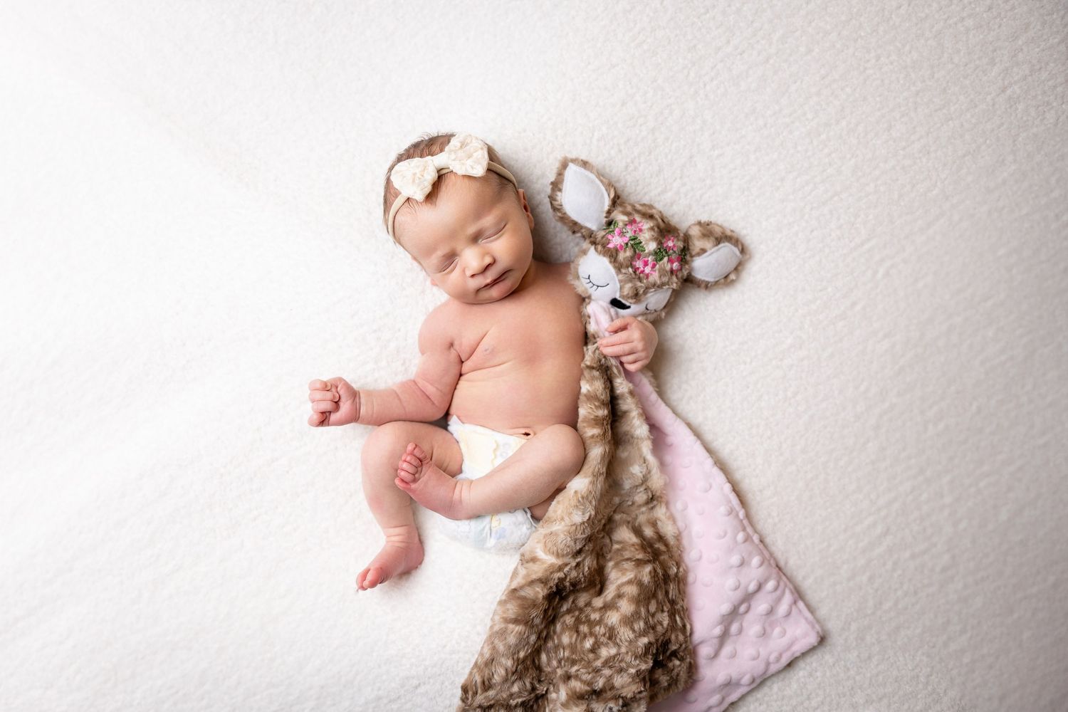 Newborn posed with plush animal toy on white blanket.