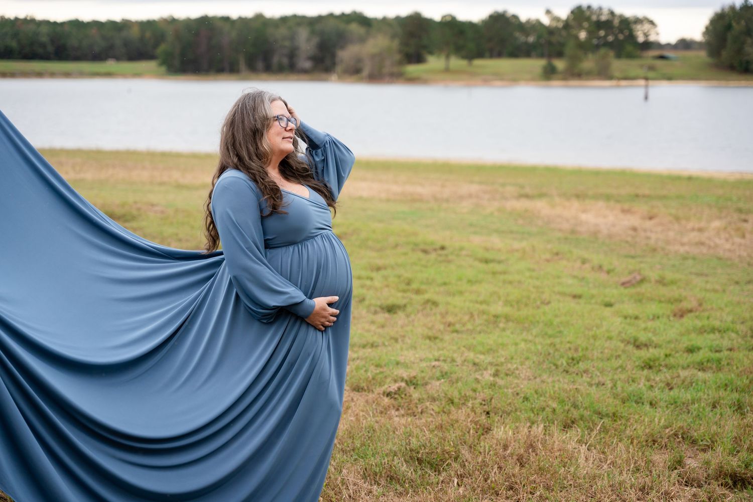 Blue dress flowing in wind against scenic lake backdrop with natural lighting.
