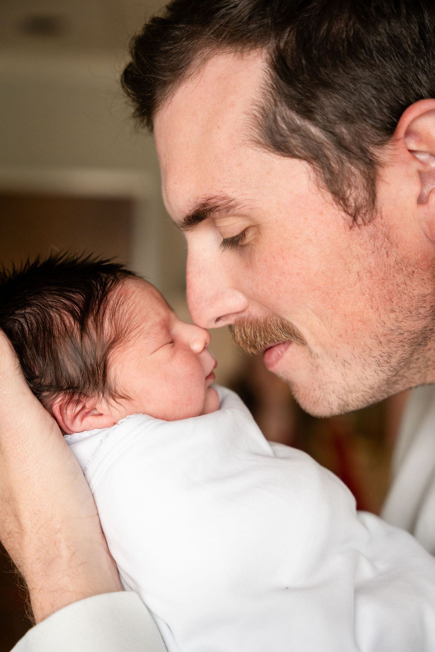 Tender moment between parent and newborn in white blanket.