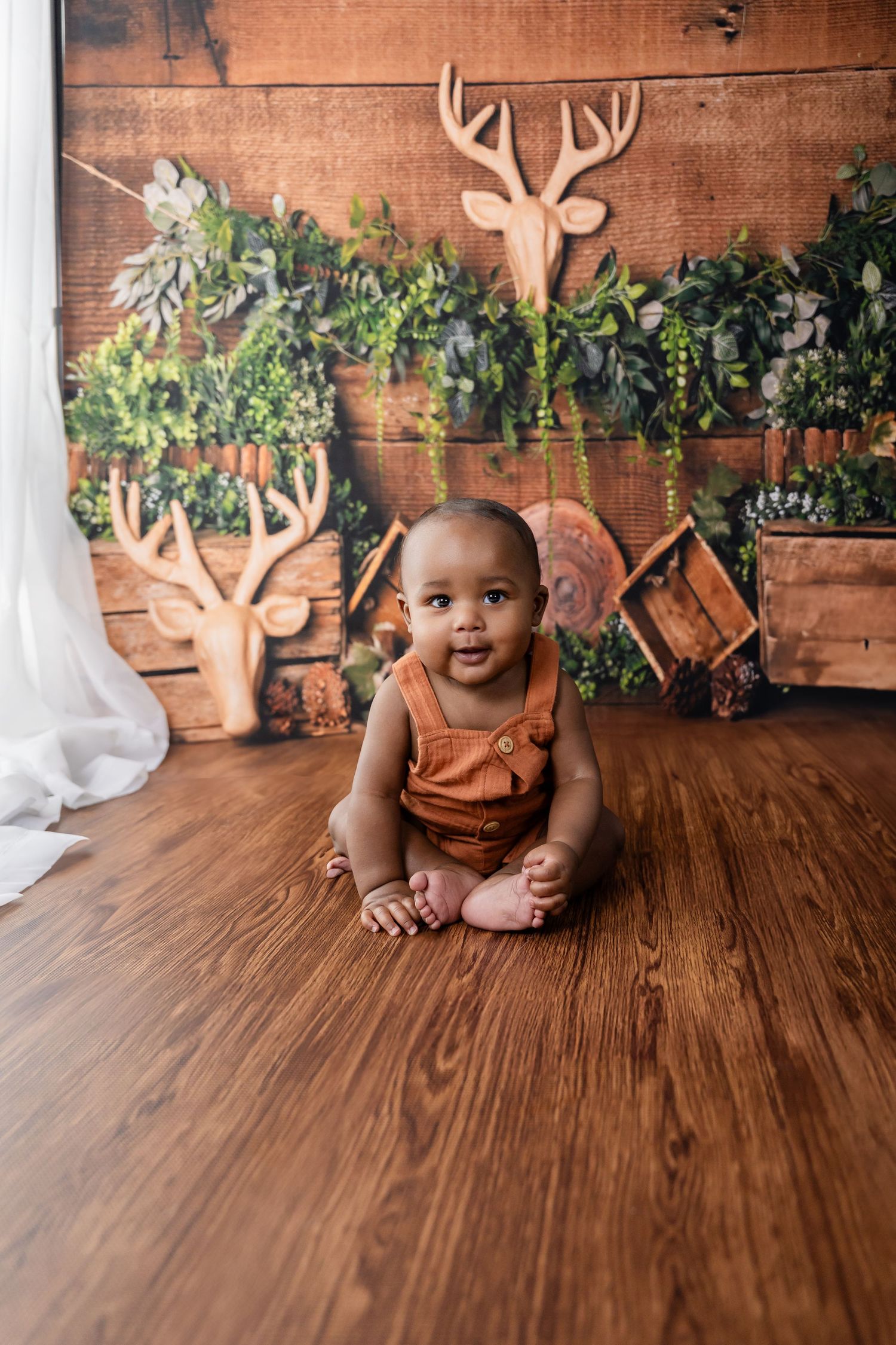 Rustic wood backdrop with antler decor and greenery on wall for baby photography session.