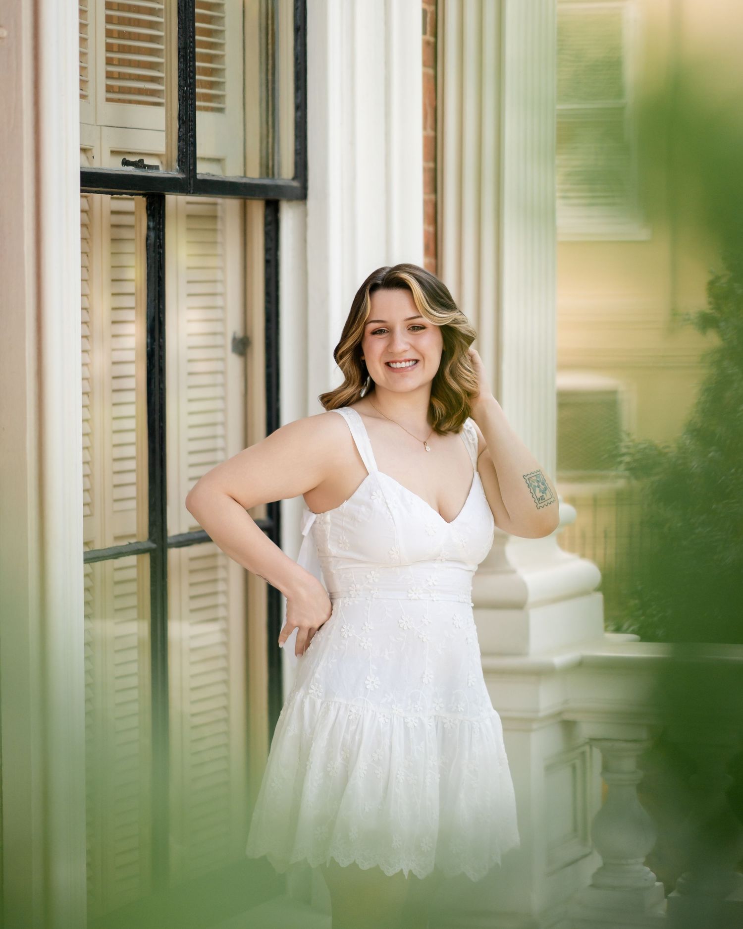 Person wearing white lace dress standing by vintage shuttered windows and white columns.