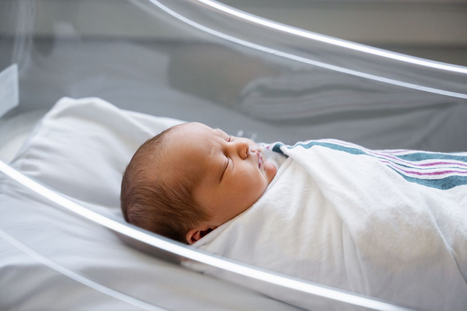 Infant sleeping wrapped in white swaddle blanket.