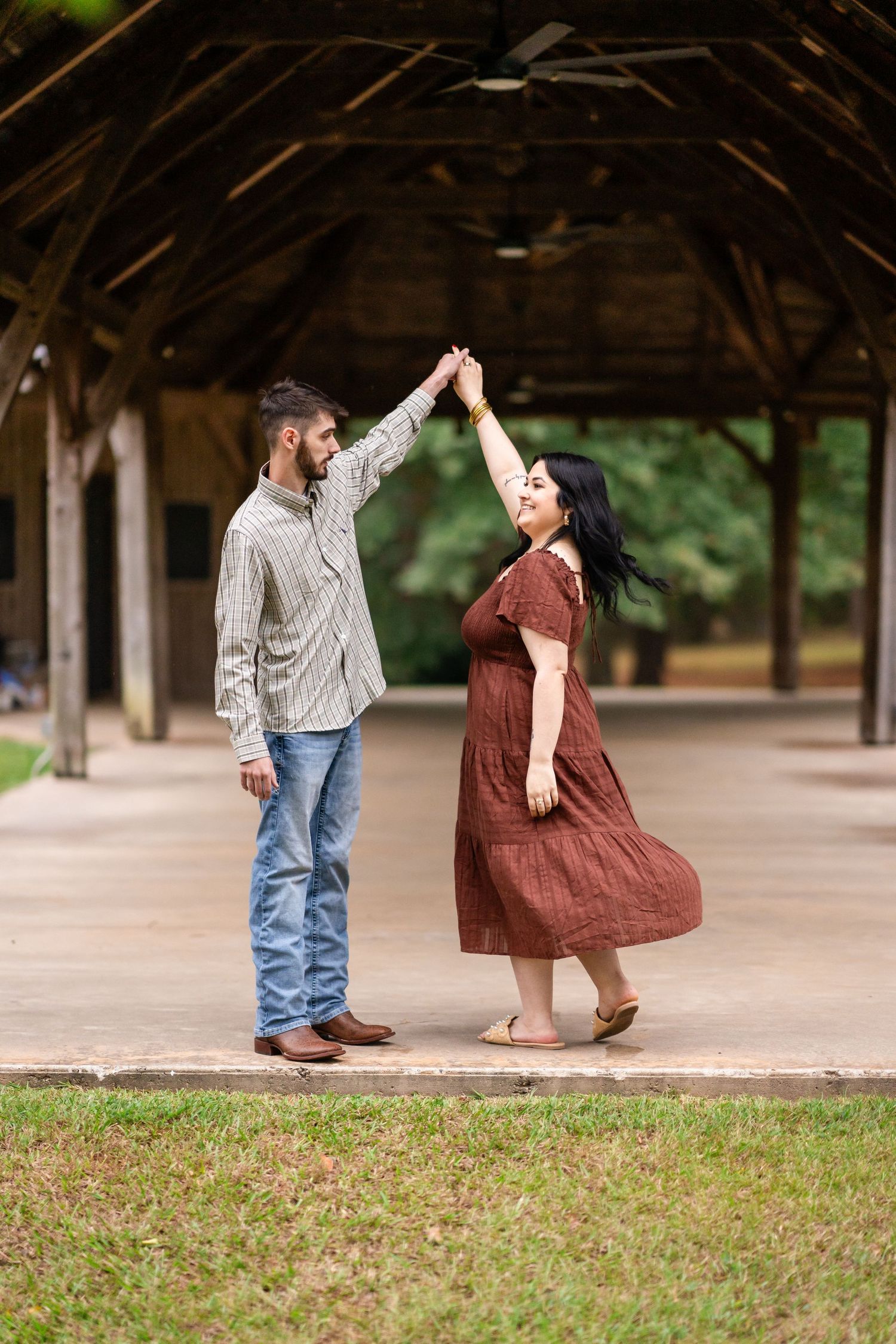 Couple dancing hand in hand as a woman in a rust dress twirls beneath her partner's raised arm under a rustic wooden pavilion.