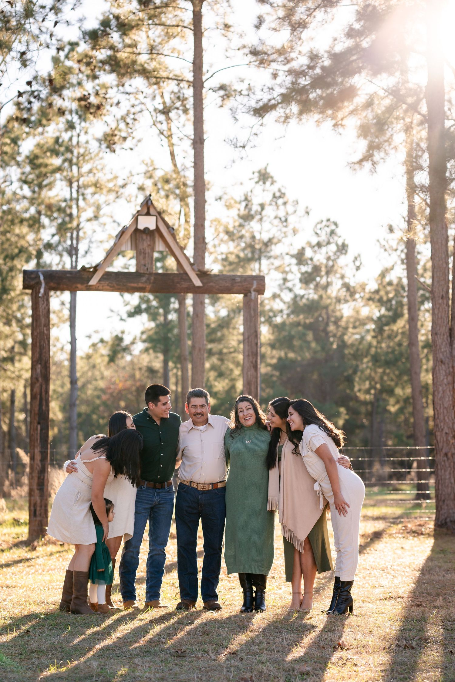 Family group stands together in casual attire against pine forest backdrop with dramatic lighting.