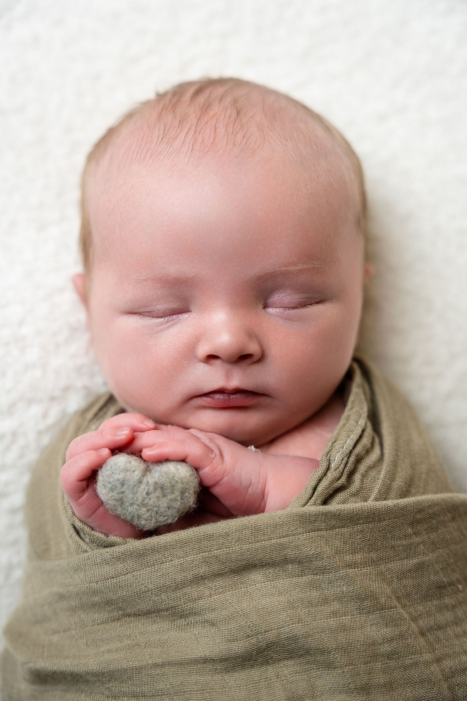 Sleeping newborn with hands visible under cozy tan swaddling cloth.