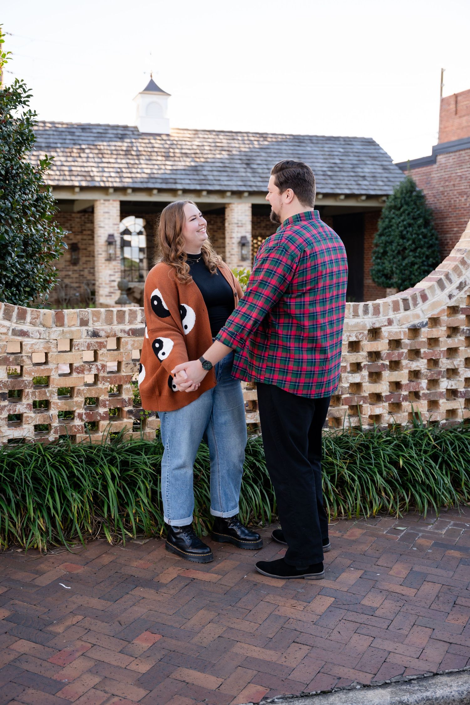 Couple posing against decorative brick wall with landscaping.