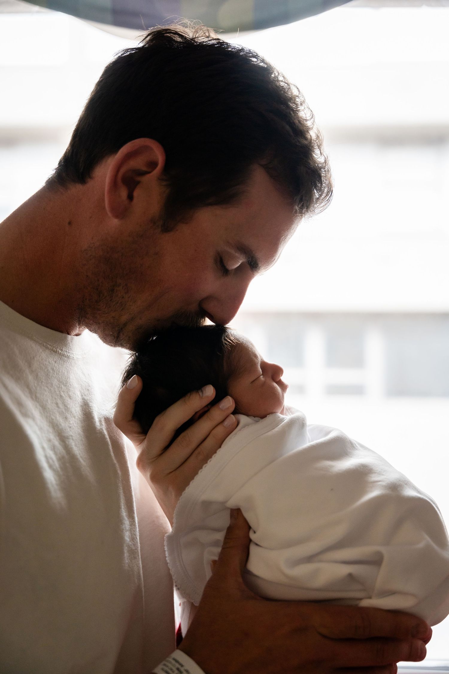 Intimate moment shared with newborn near bright window.