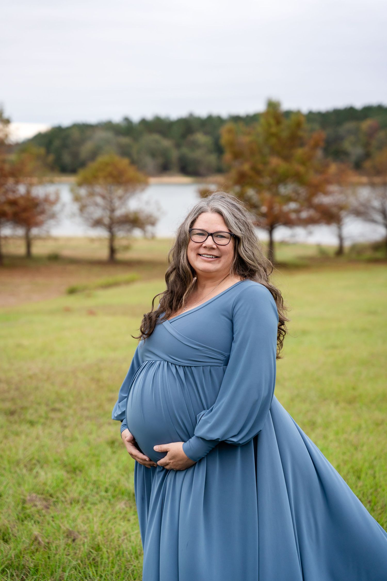 Joyful solo maternity portraits in flowing blue dress against natural landscape.