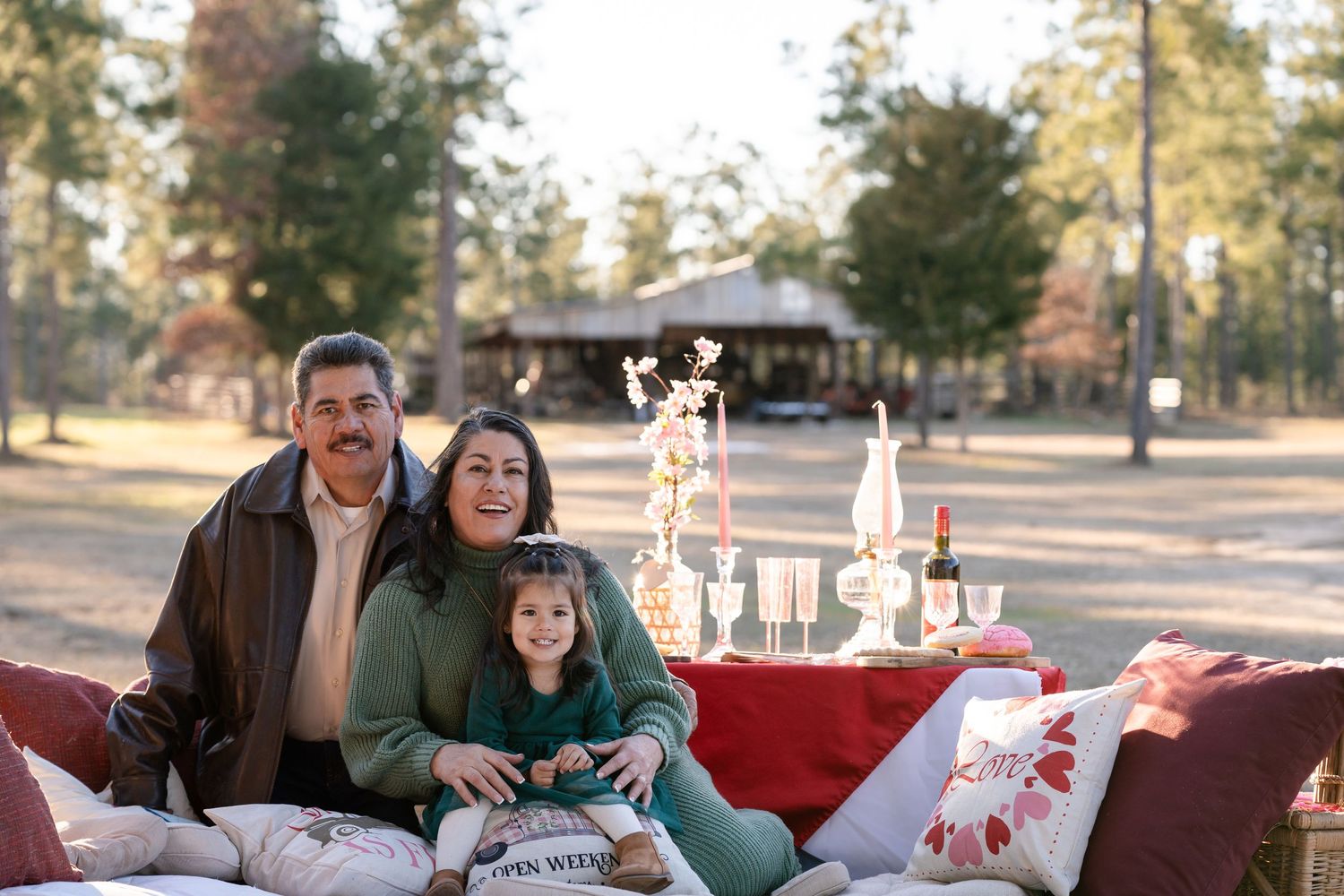 Family lounging on picnic blanket with vintage decor in natural setting.