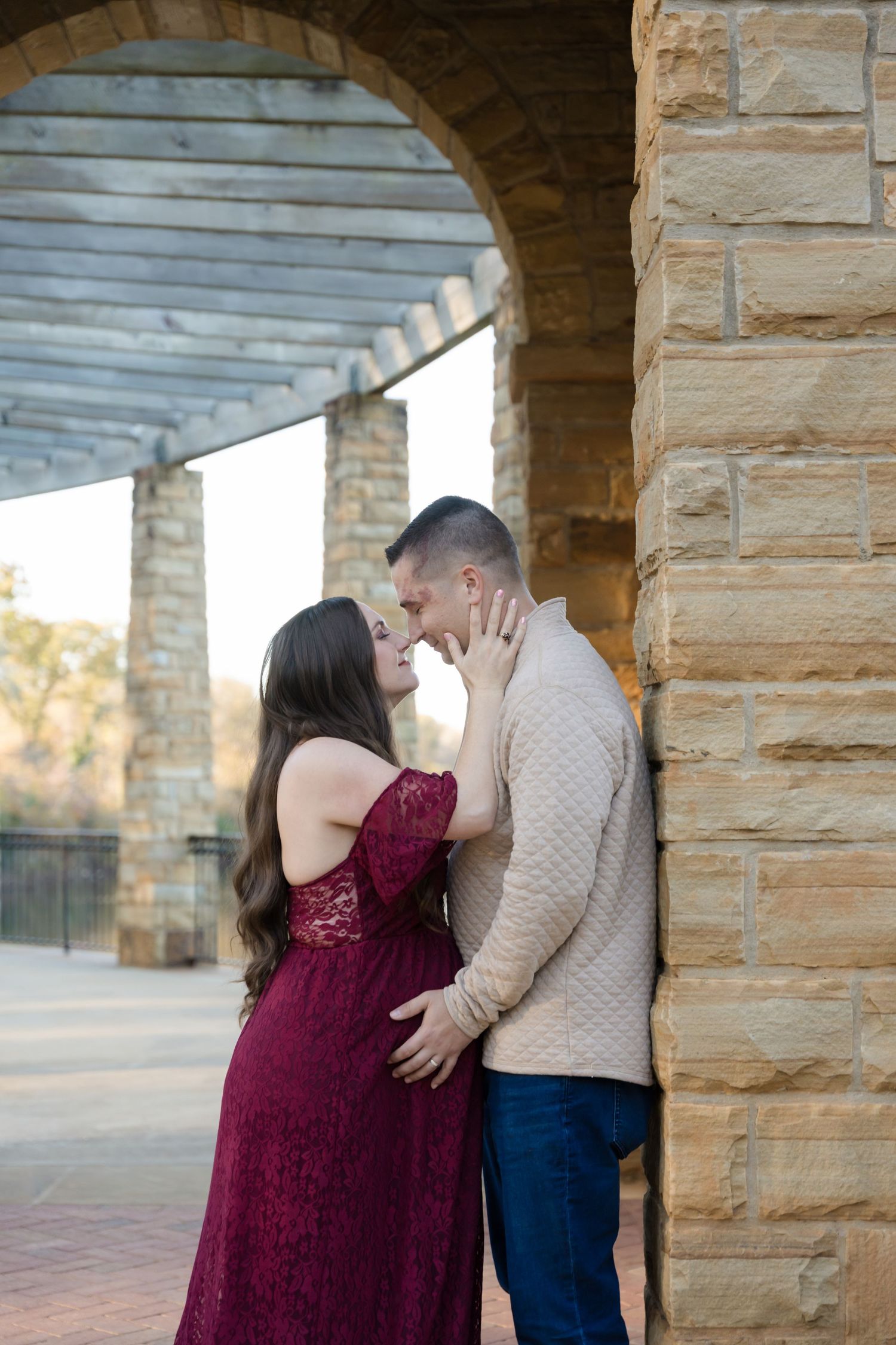 A couple shares an intimate moment under a stone archway in a romantic outdoor setting.