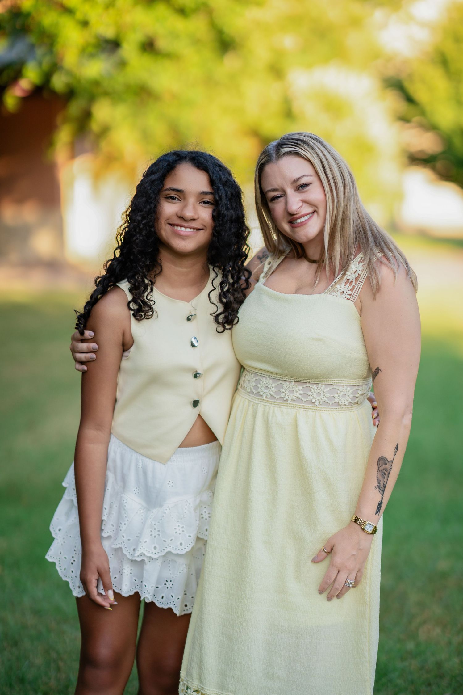 Two women in yellow outfits smiling together outdoors in a lush green park setting.