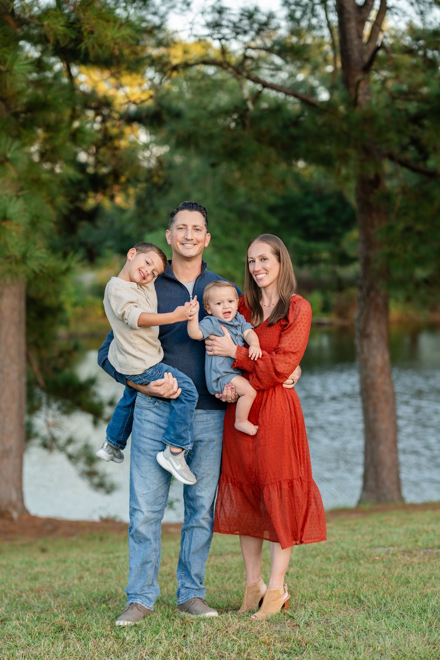Family enjoying a casual outdoor photoshoot by a lake on a sunny autumn afternoon.