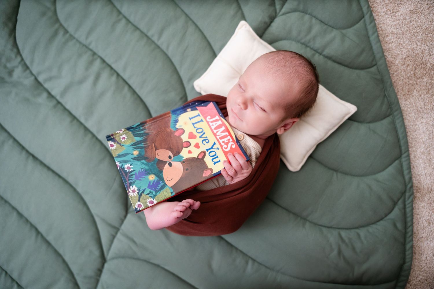 Sleeping newborn on green quilted blanket with children's book and small white pillow.