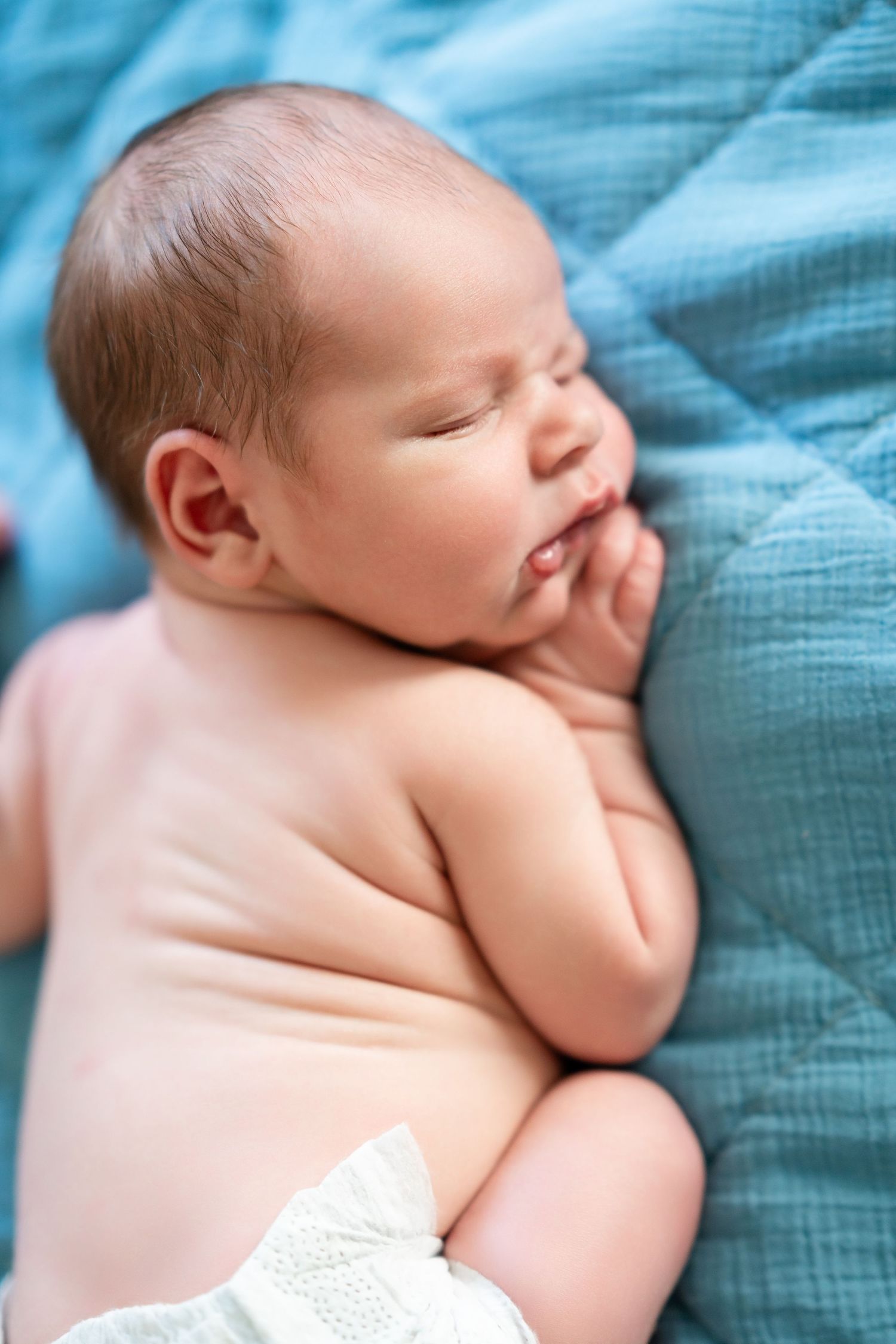 Sleeping newborn baby on turquoise bedding in peaceful pose.