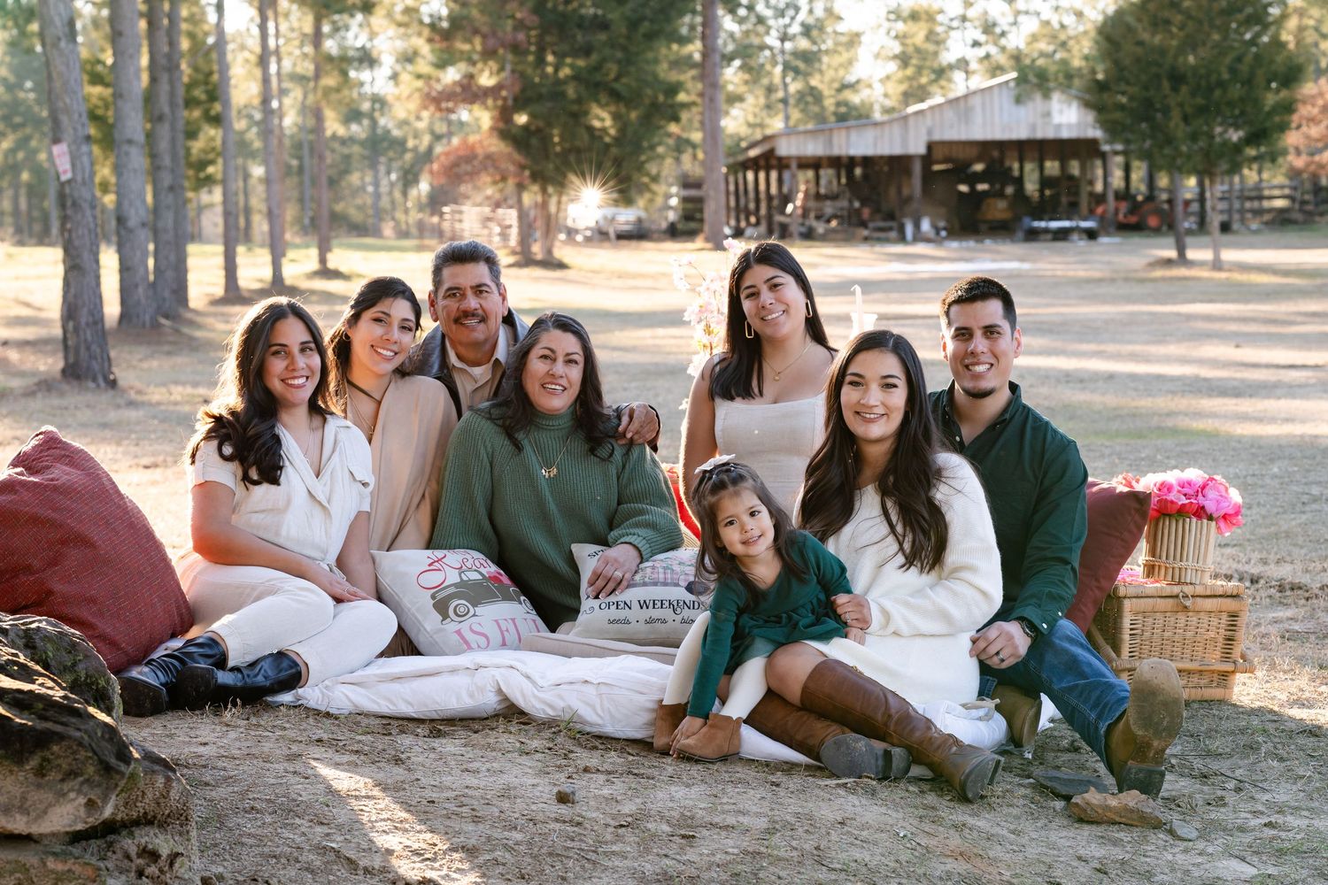 A group lounges on blankets for an outdoor picnic gathering in a pine forest setting.