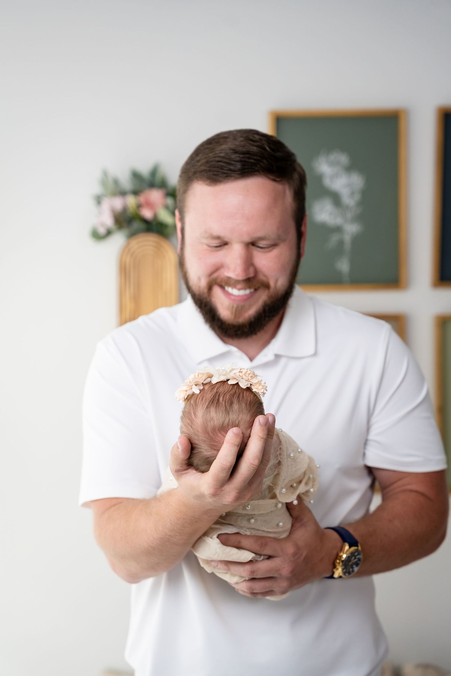 Man in white polo shirt holding newborn baby with genuine joy against light background.