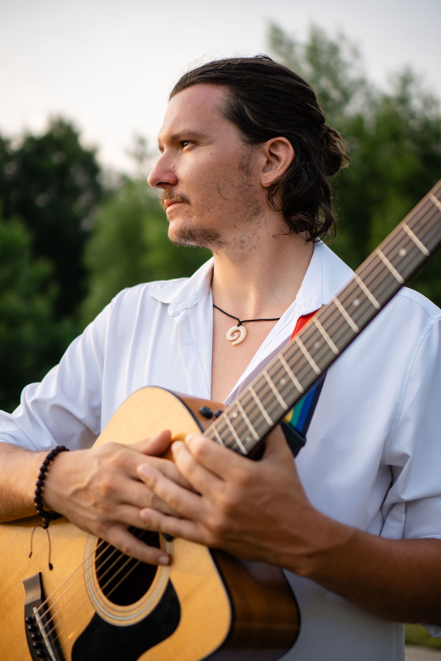 Musician playing acoustic guitar while wearing white shirt outdoors.