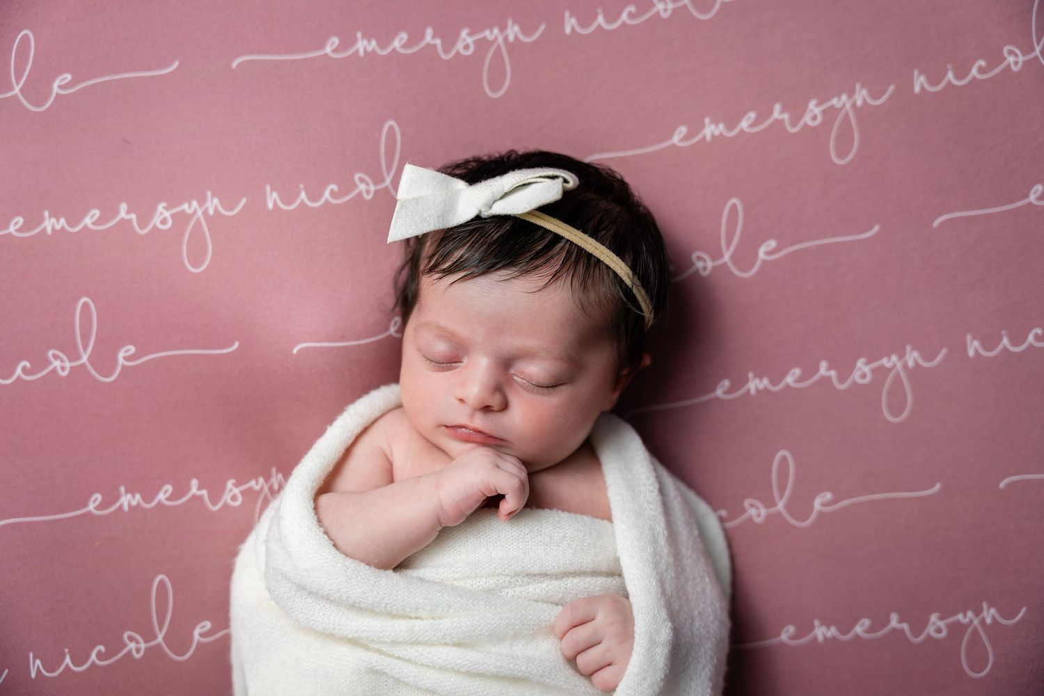 Newborn baby sleeping peacefully on white blanket with soft pink background and cursive text overlay.