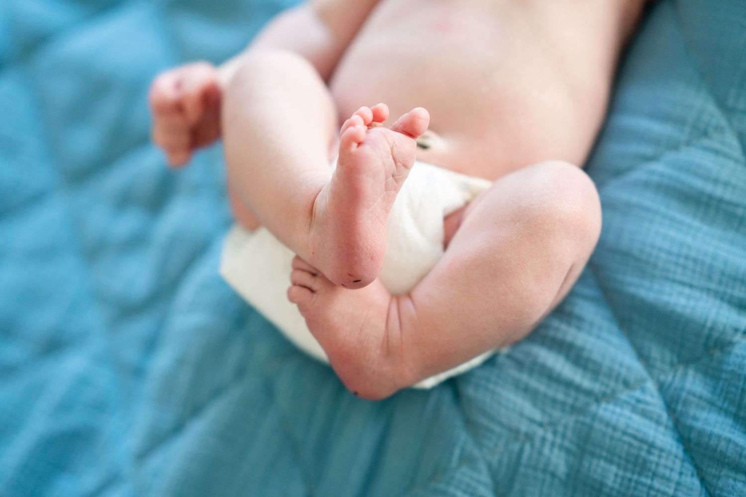 Tiny baby feet and toes against soft blue textured background.
