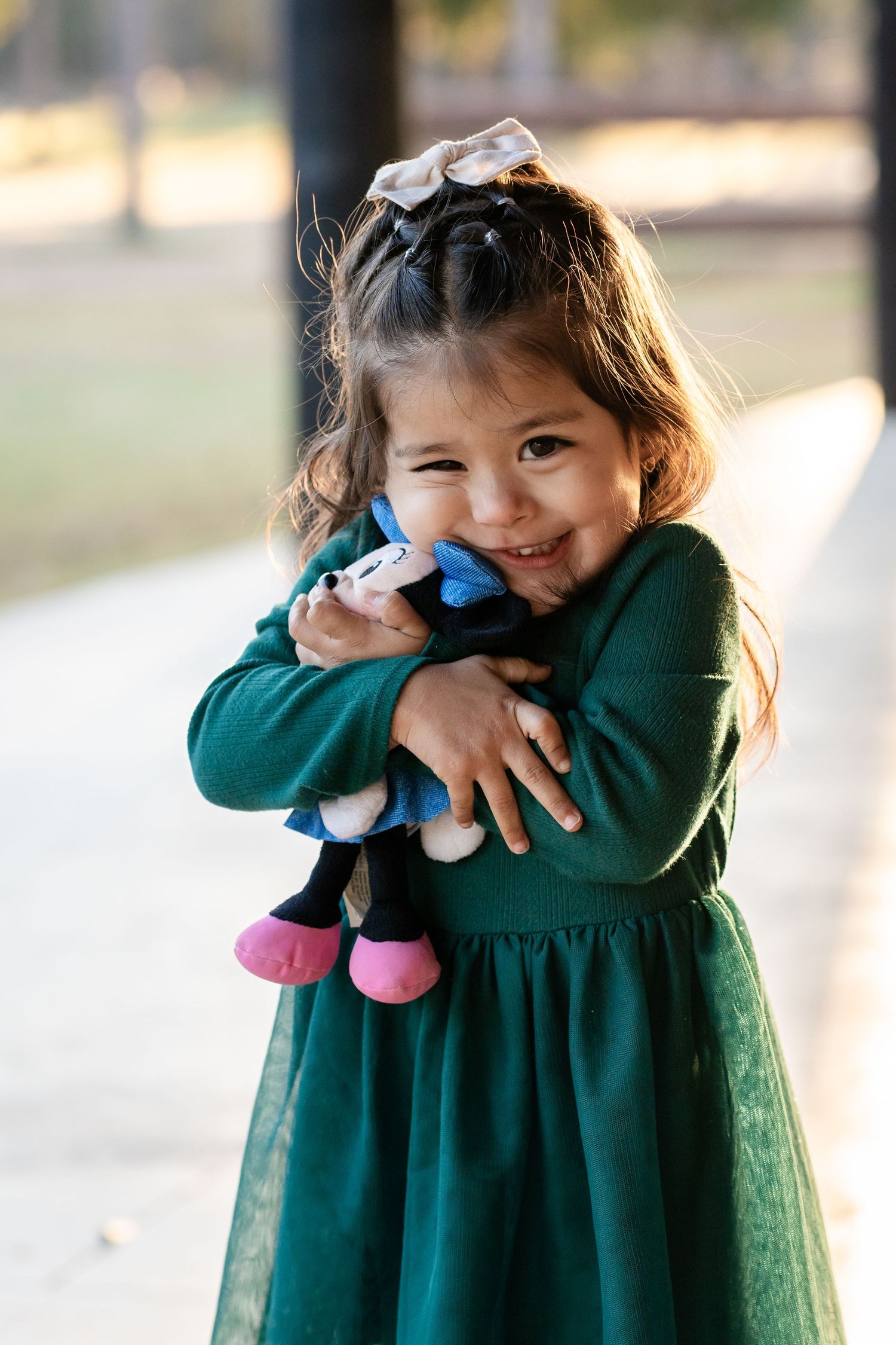 A small child in a green dress hugs a plush toy while smiling at the camera.
