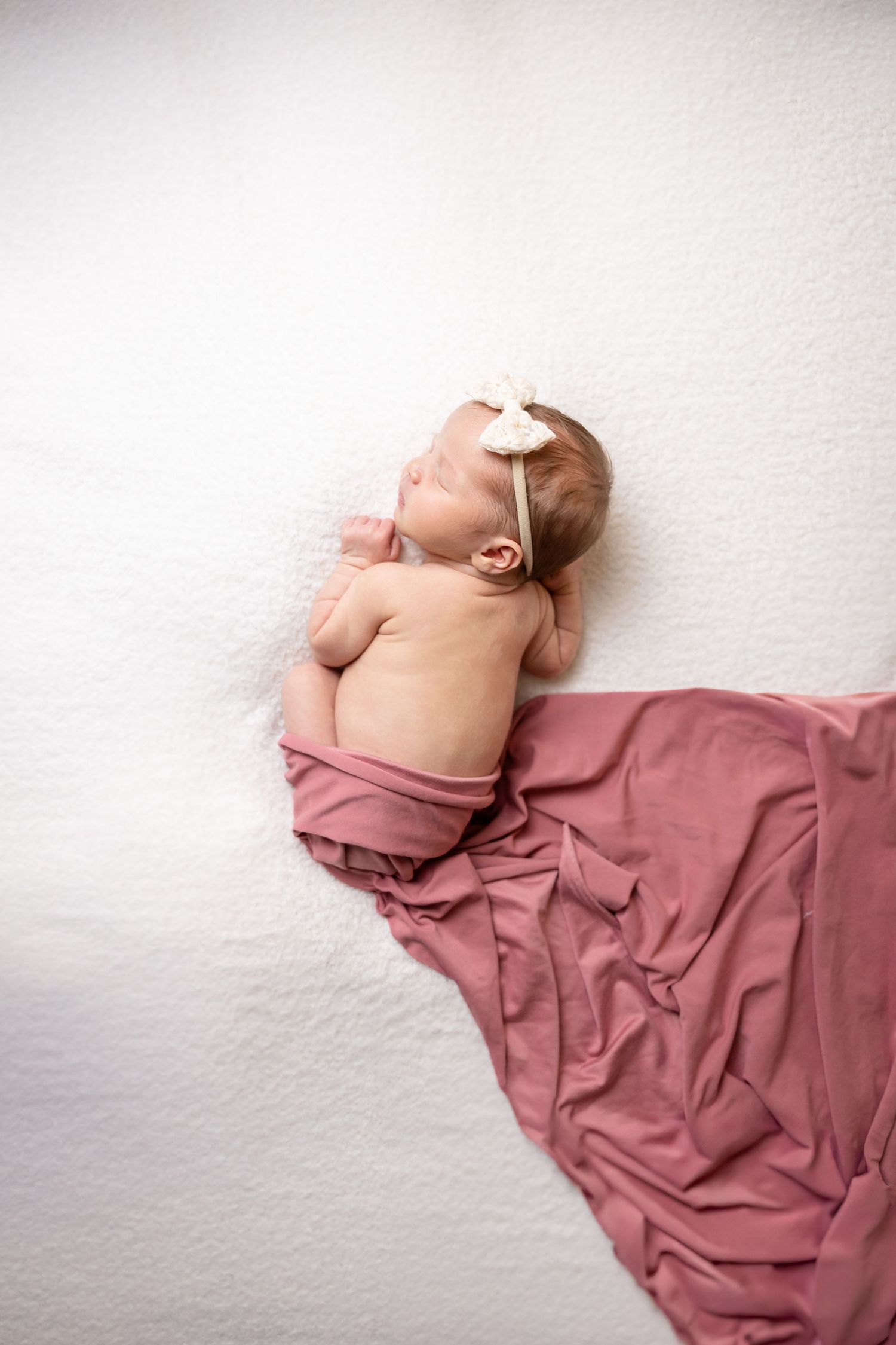 Side profile of baby wrapped in mauve fabric against white backdrop.