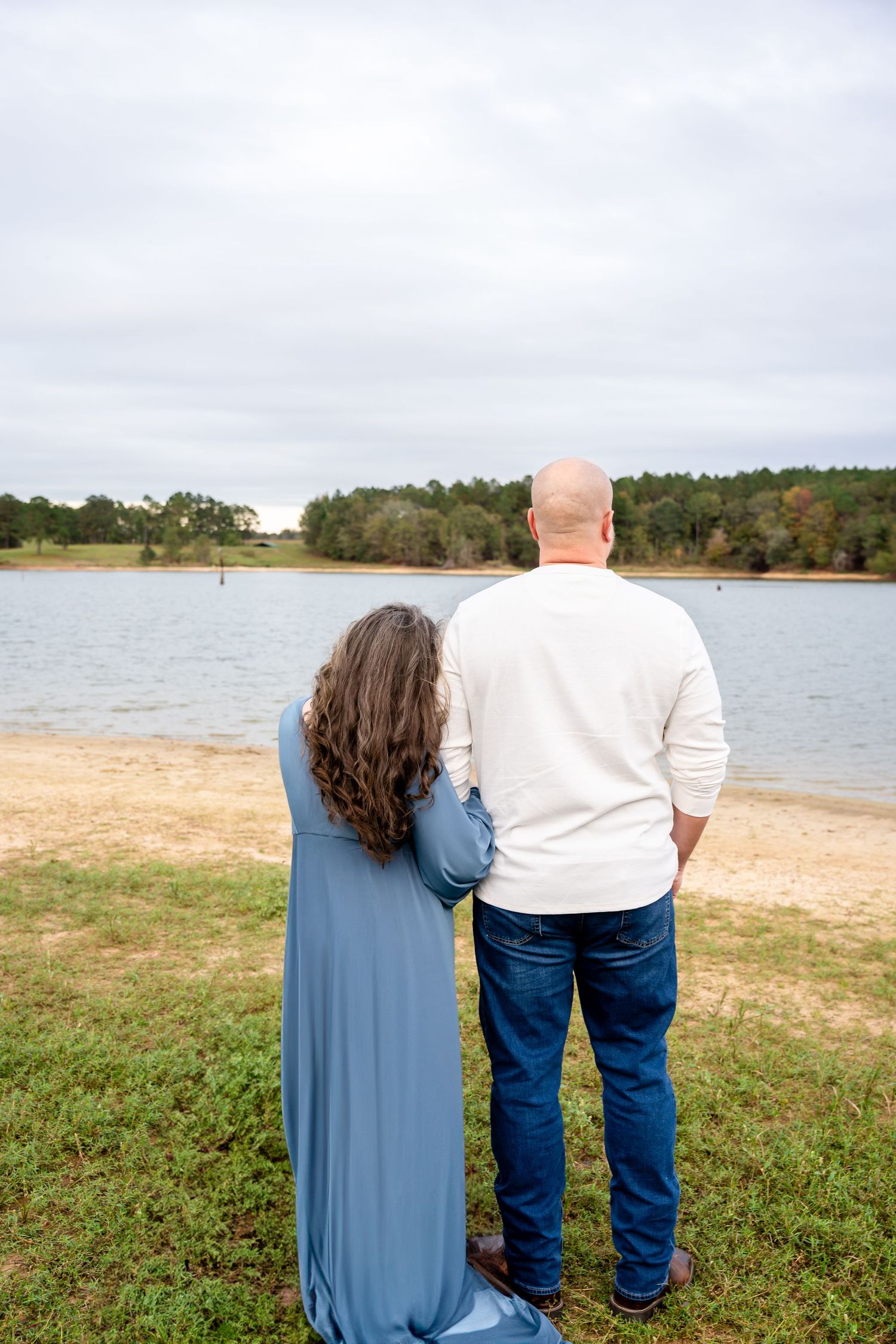Couple stands together looking out over peaceful lake view on cloudy afternoon.