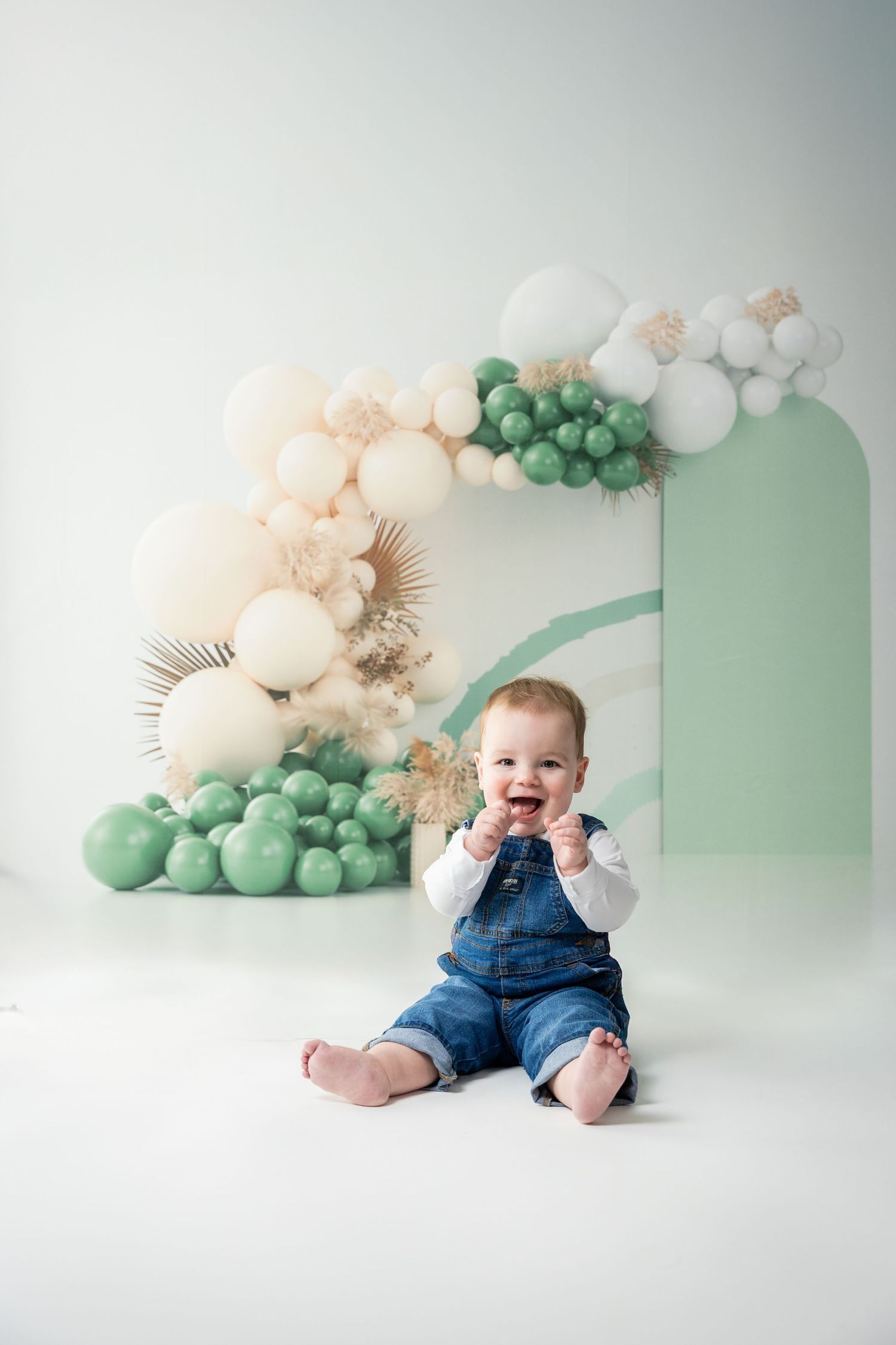 Professional baby photography setup with mint green and peach balloon garland decorations against white backdrop.