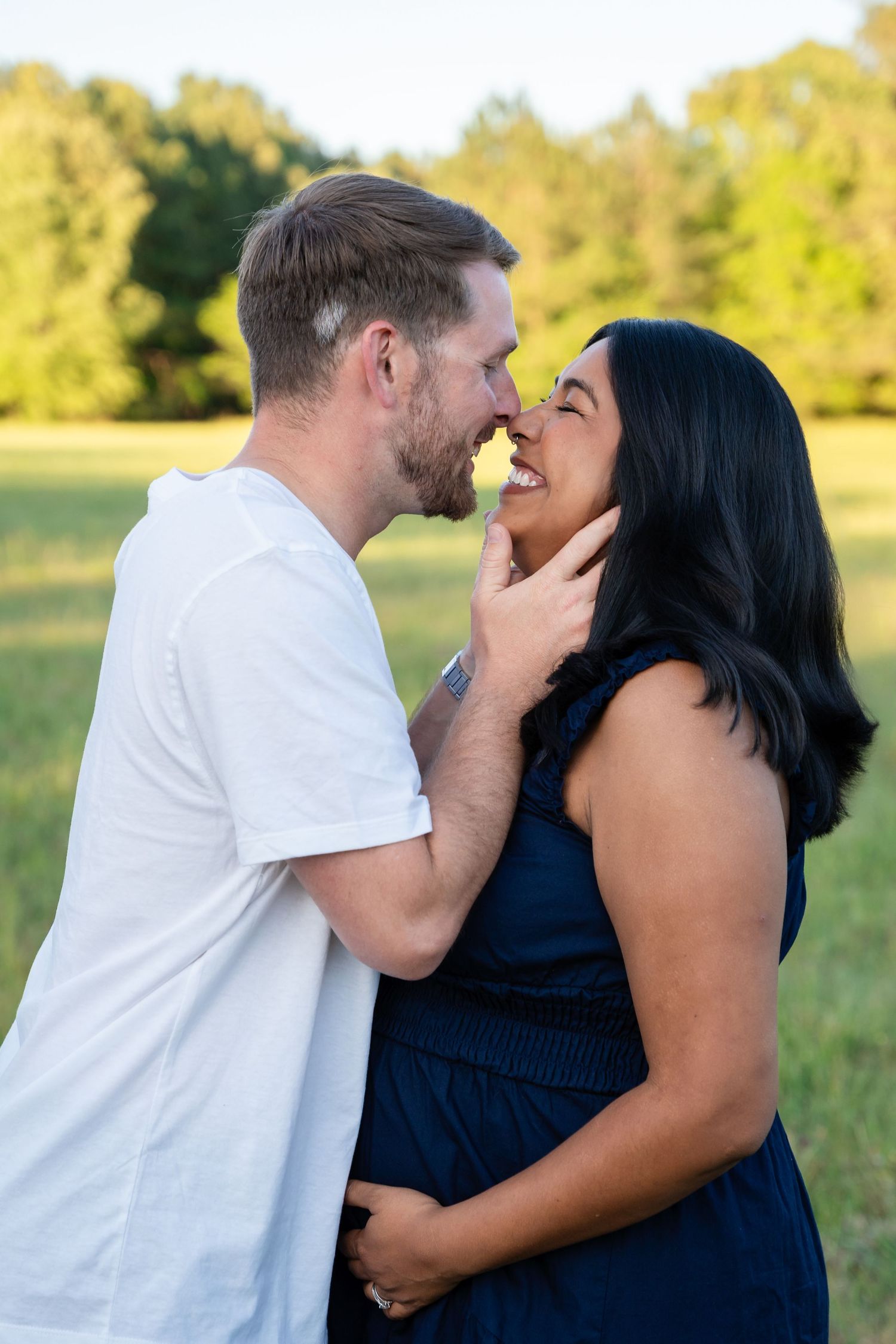 A happy couple sharing a romantic moment outdoors, smiling face-to-face in a sunny green field.
