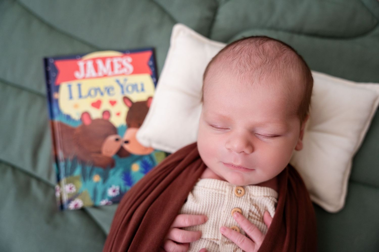 Peaceful sleeping newborn with children's book on green quilted background.