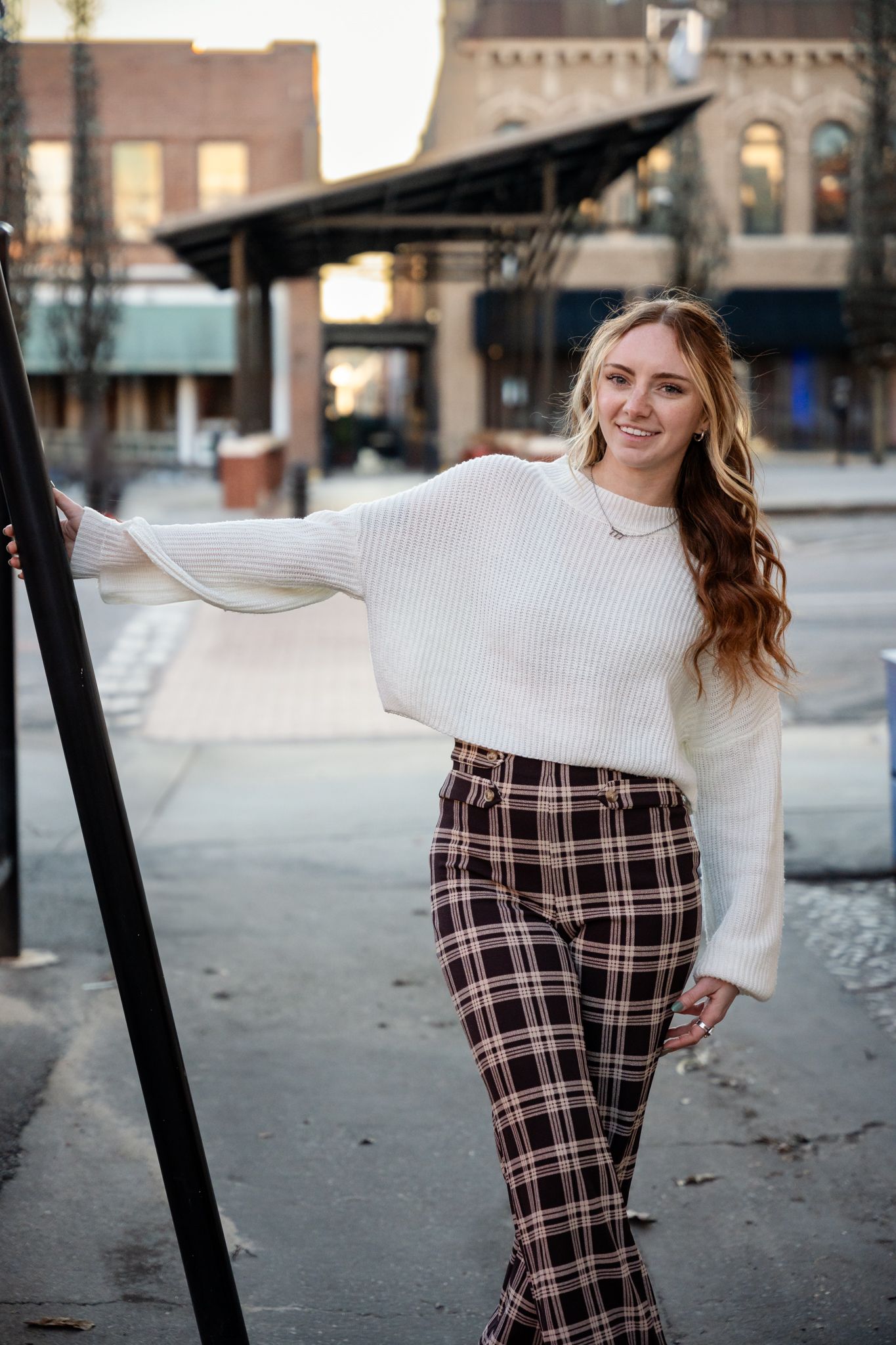 Fashion portrait of someone wearing a cozy cream sweater and plaid pants posing against an urban backdrop.