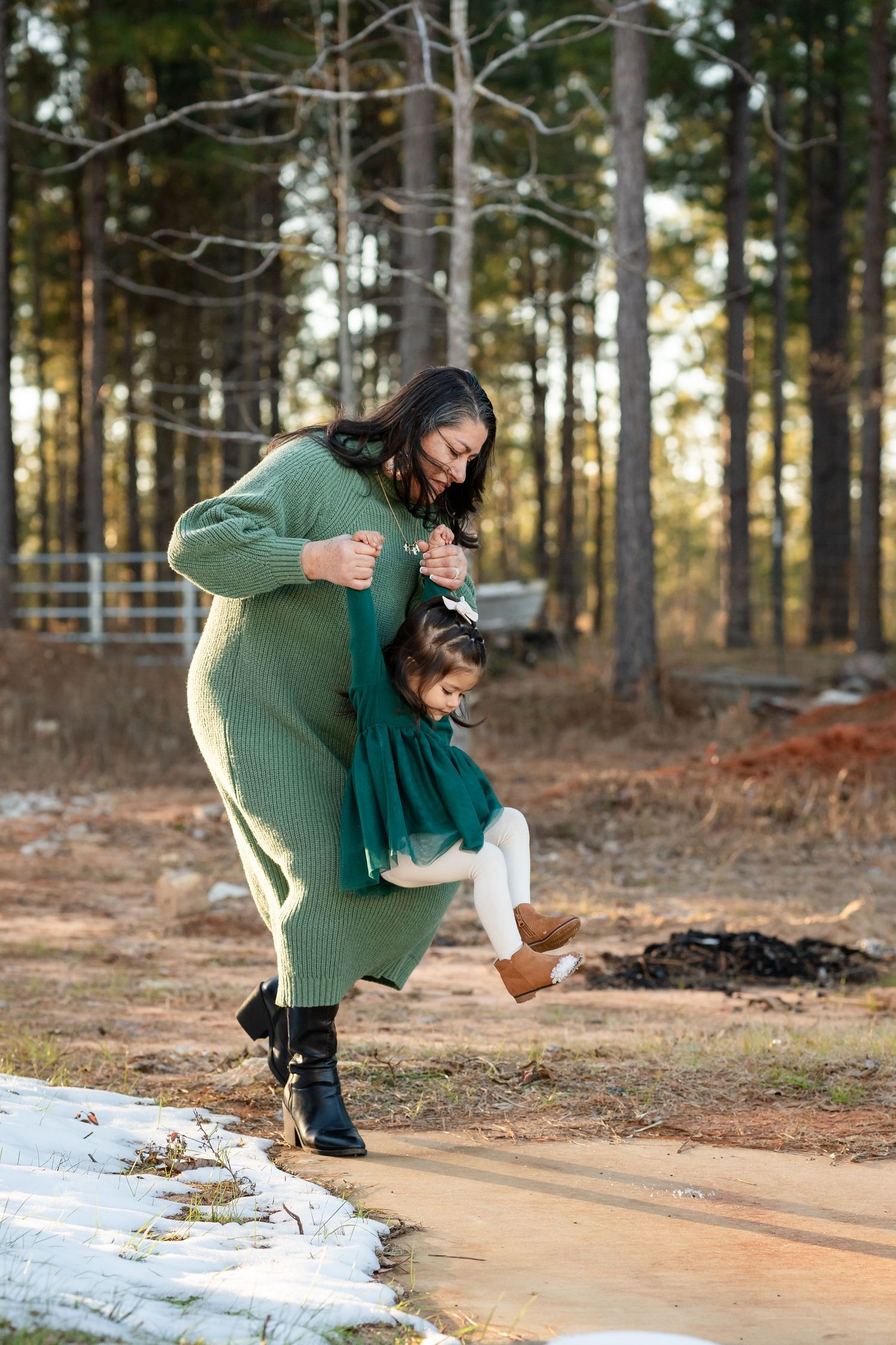 A playful moment in the forest with matching green outfits and snow on the ground.